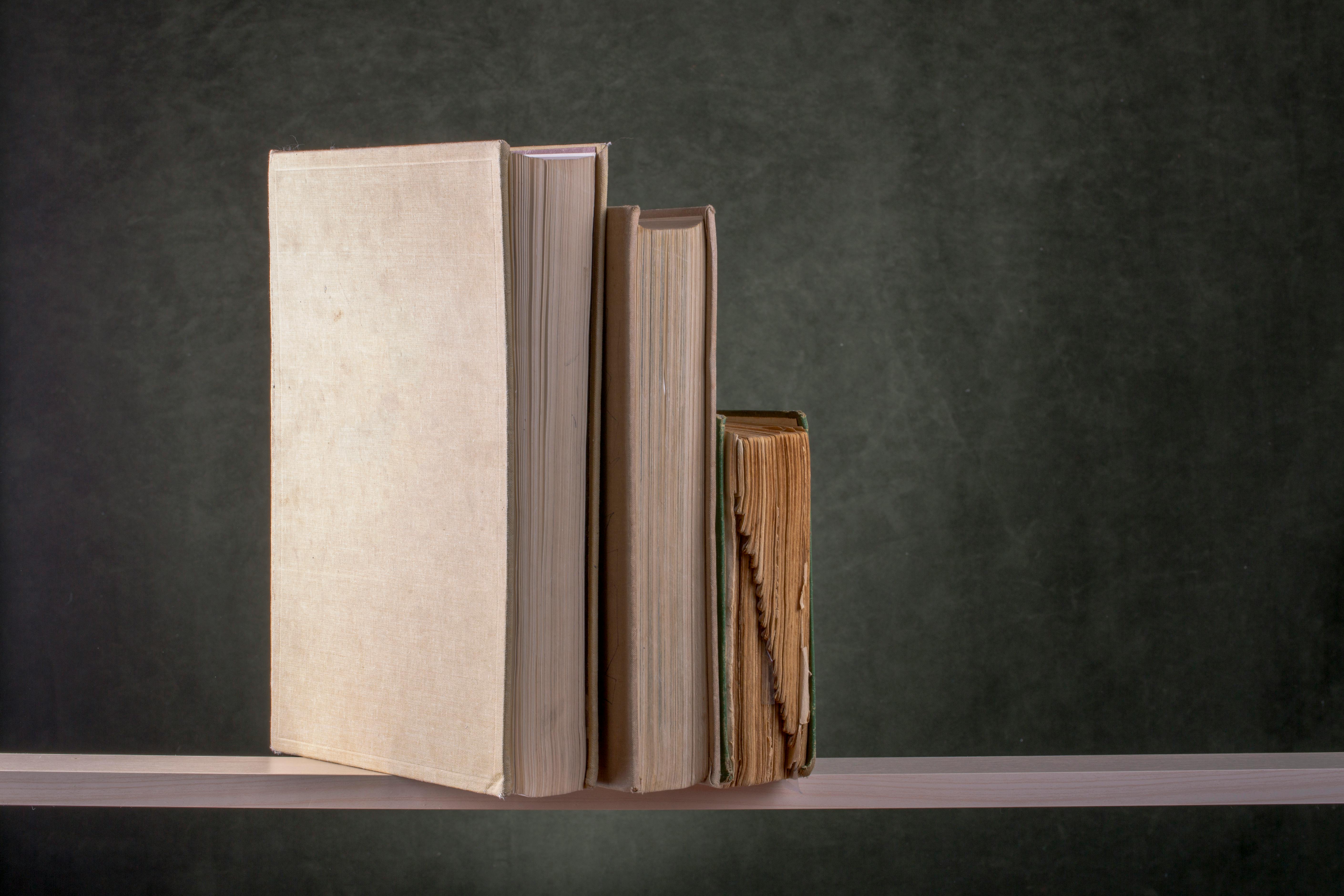 Zadarmo Tri staré knihy stojace na drevenej poličke na tmavom pozadí, evokujúce vintage atmosféru. Fotka z fotobanky