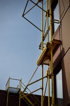 Yellow scaffolding on a modern building facade in natural light against a clear sky.