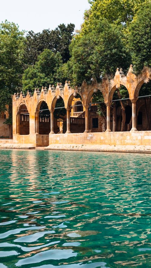 Free A serene scene of historic stone arches reflected in calm waters with lush greenery. Stock Photo