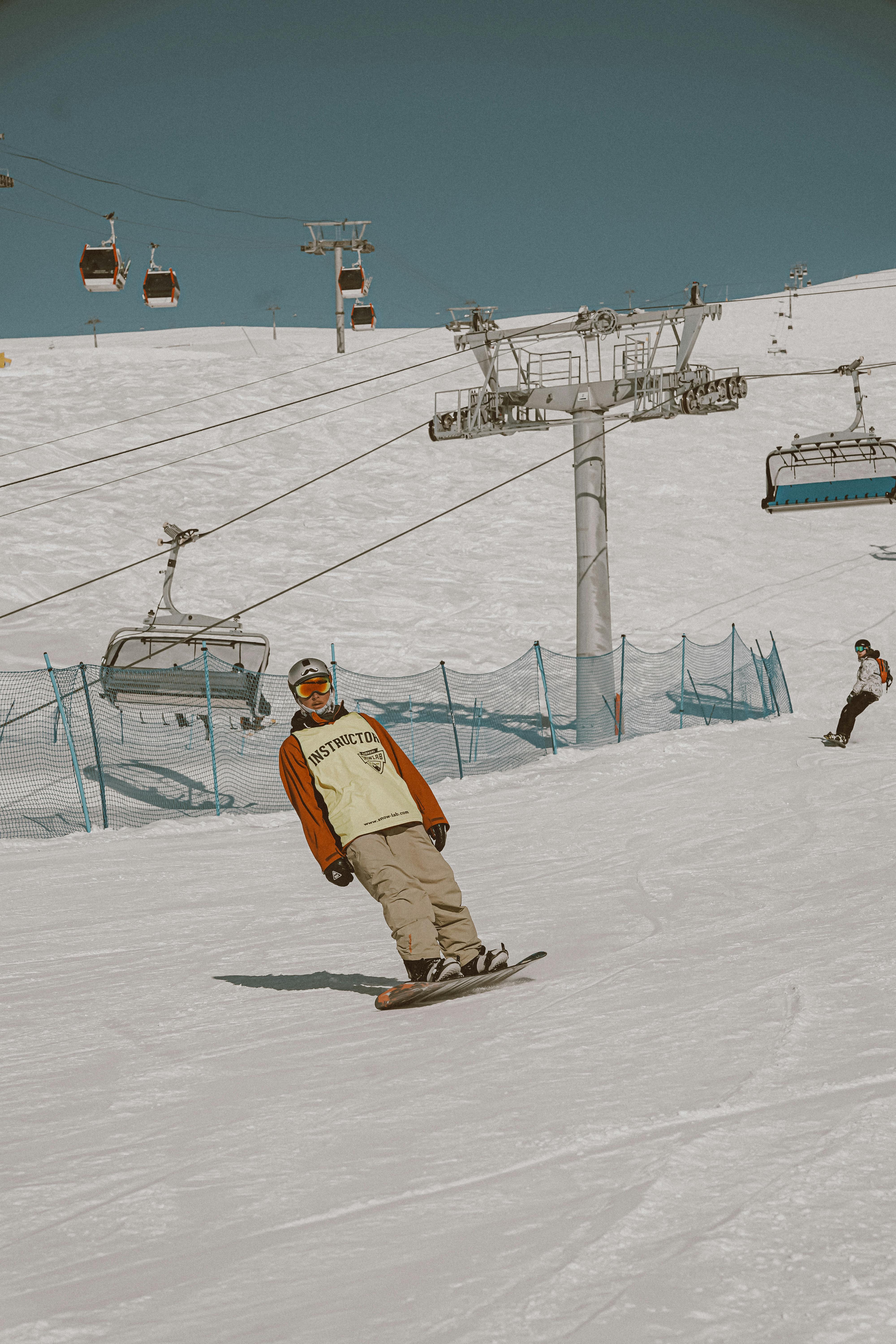Dynamic snowboarder gliding down a snowy slope under a clear blue sky with ski lifts in the background.