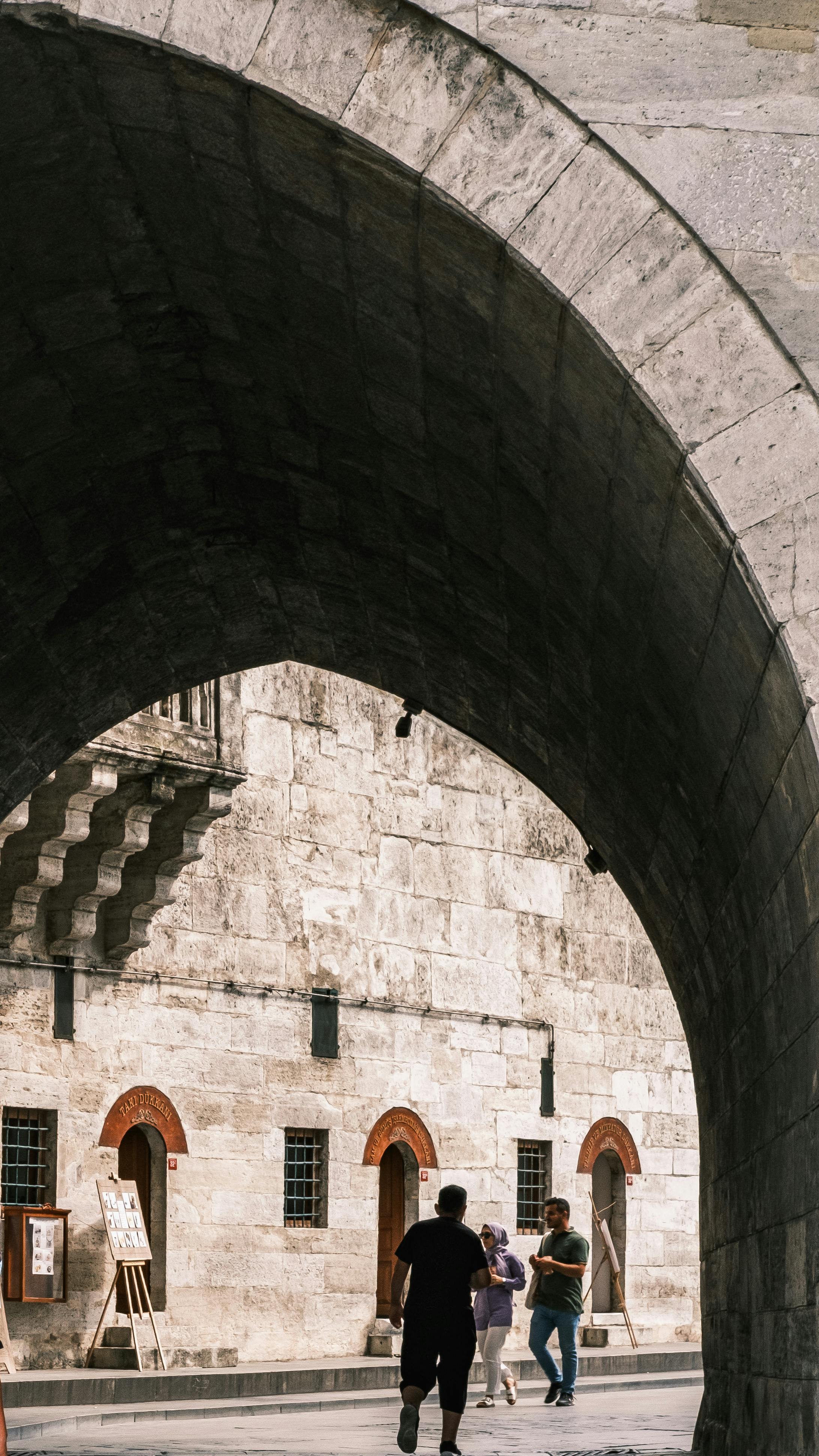 ingyenes Emberek sétálnak át egy történelmi kőboltíven egy napsütéses napon, megörökítve a város felfedezését. Stockfotó