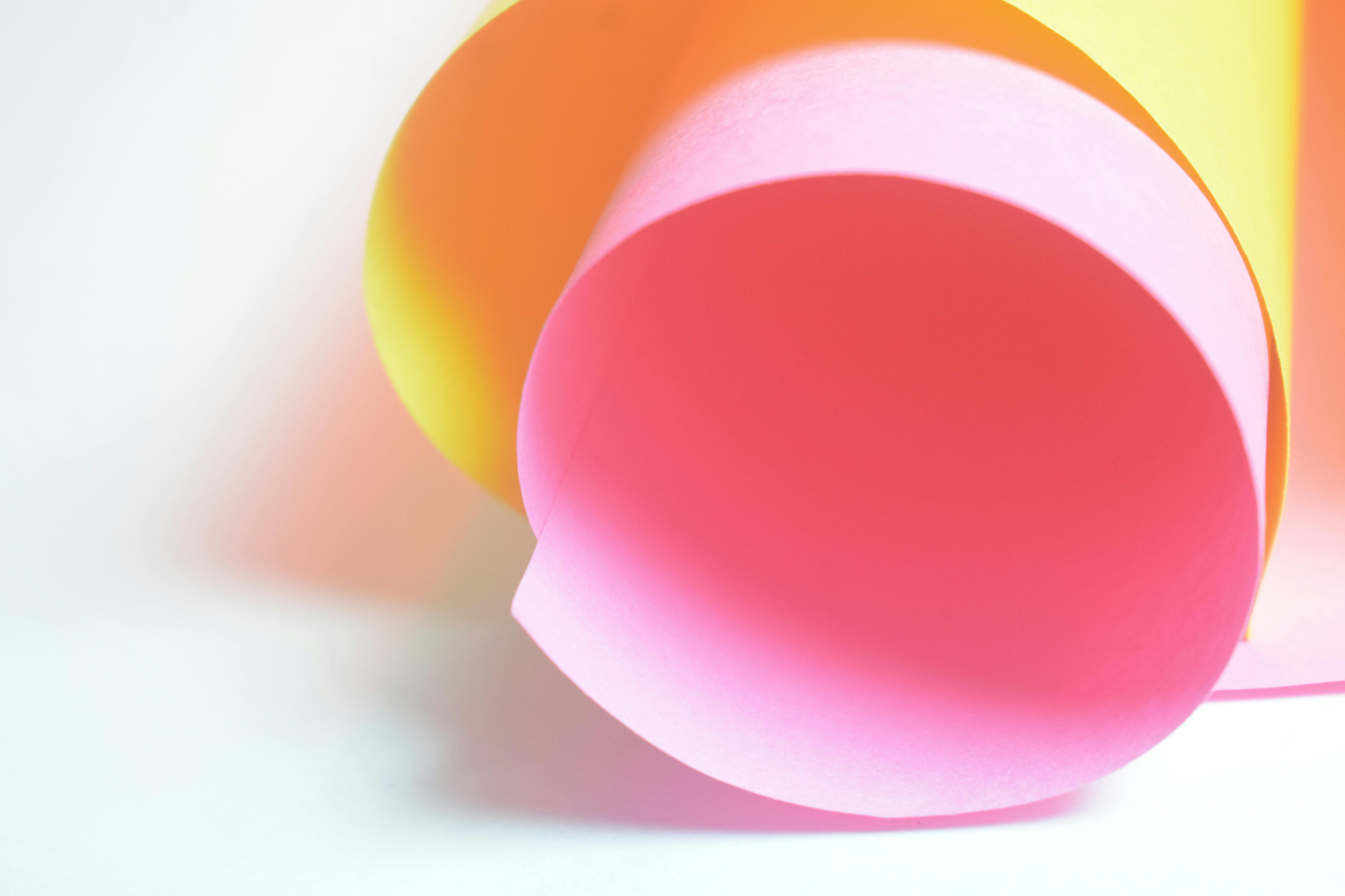 Gratis Una vivace composizione astratta con carta arrotolata rosa e gialla e luci soffuse. Foto a disposizione