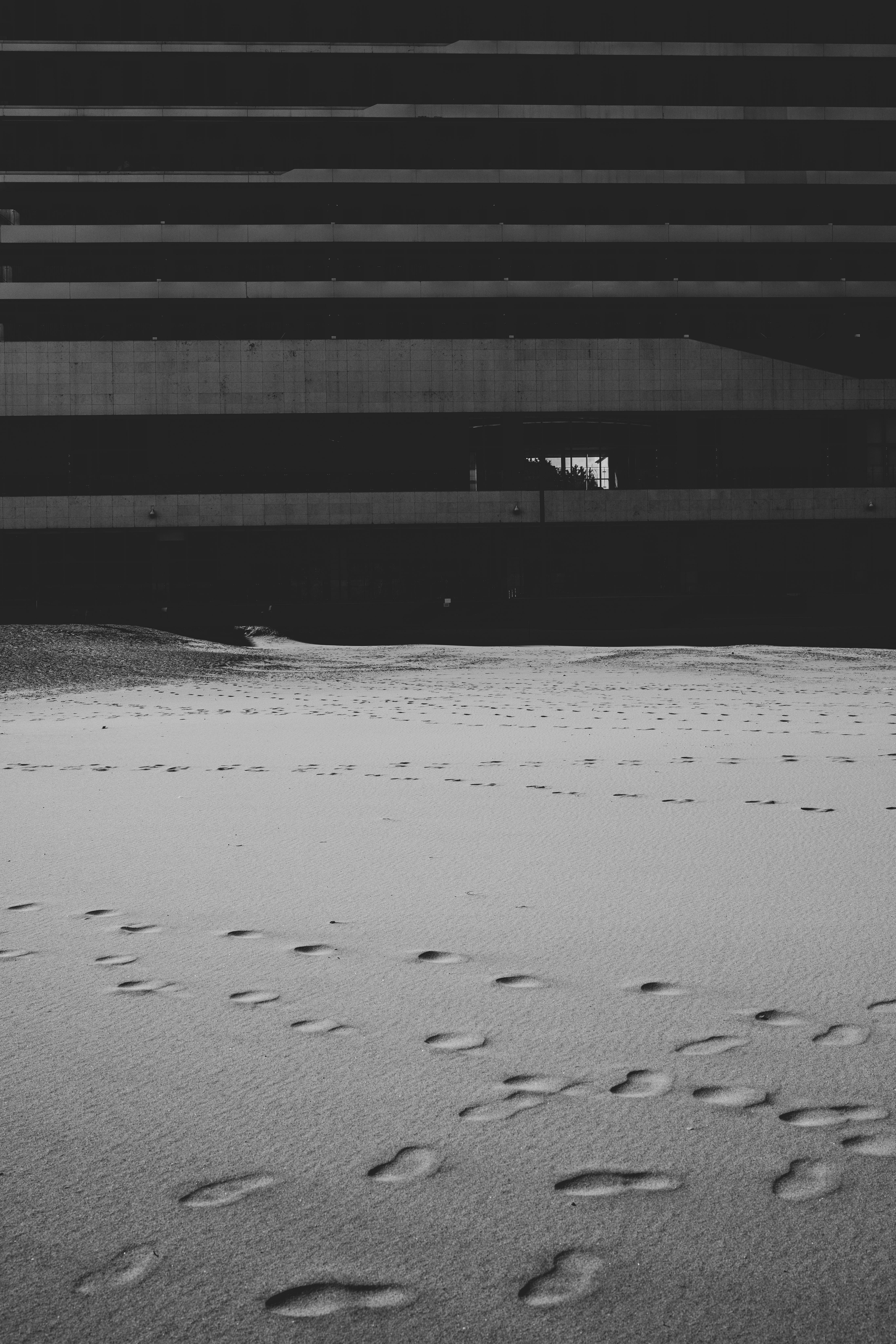 Gratis Imagen monocromática de huellas en una playa de arena frente a un edificio moderno bajo un cielo nublado. Foto de stock