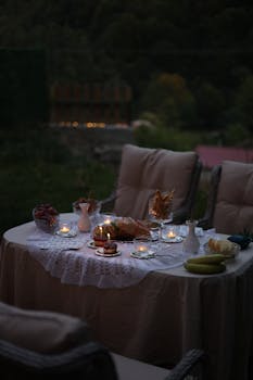 Cozy outdoor dining table decorated with candles and snacks at twilight, creating a warm, inviting atmosphere.