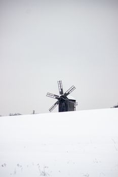 A solitary windmill stands on a snow-covered landscape under a grey winter sky.
