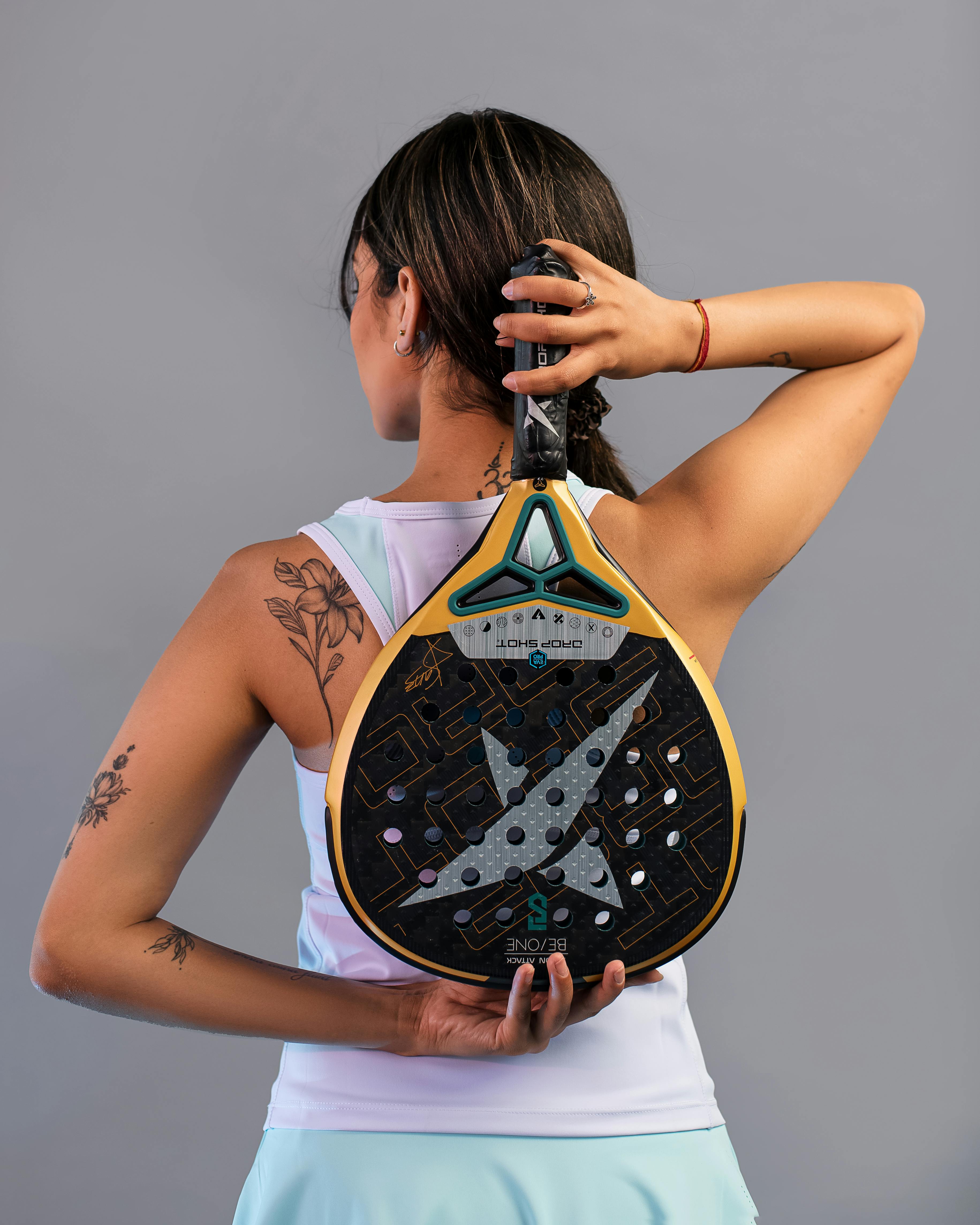 ingyenes Egy női sportoló hátulnézete, aki padel ütőt tart a kezében, tetoválásokat és sportos öltözéket mutat. Stockfotó