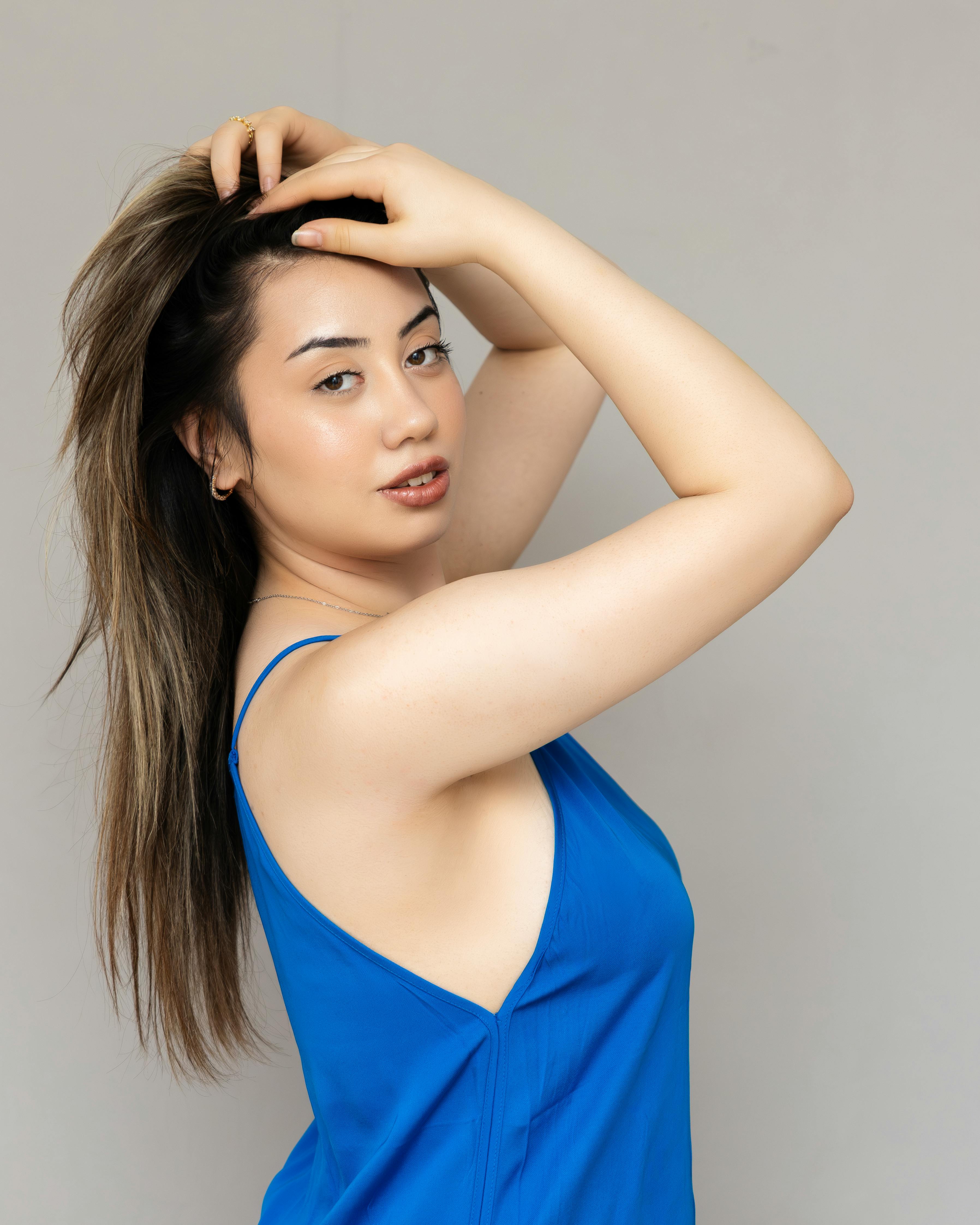 Gratis Elegante ritratto di una donna con capelli lunghi e abito blu su sfondo neutro. Foto a disposizione