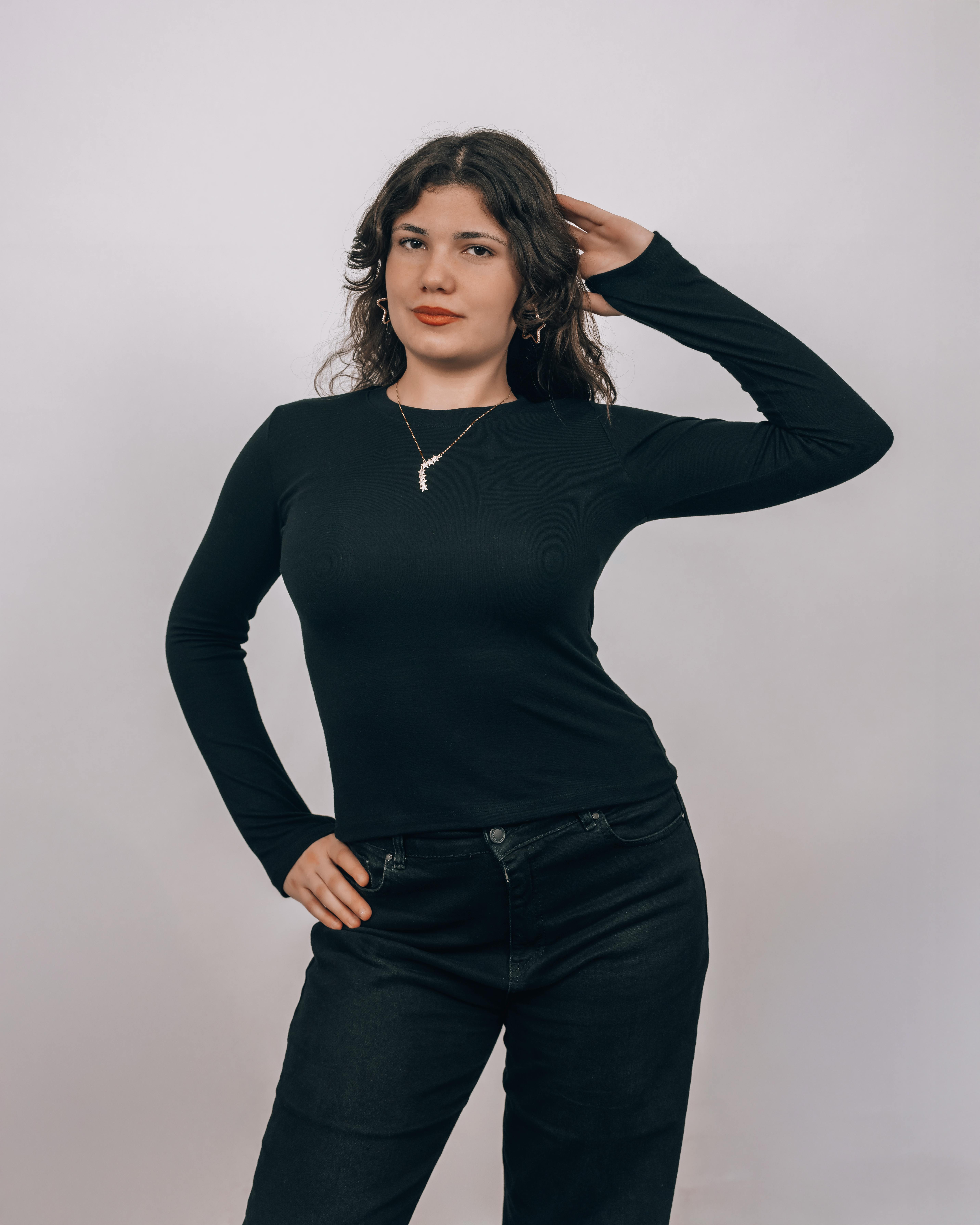 Free A confident woman in a black outfit poses stylishly against a neutral studio background. Stock Photo