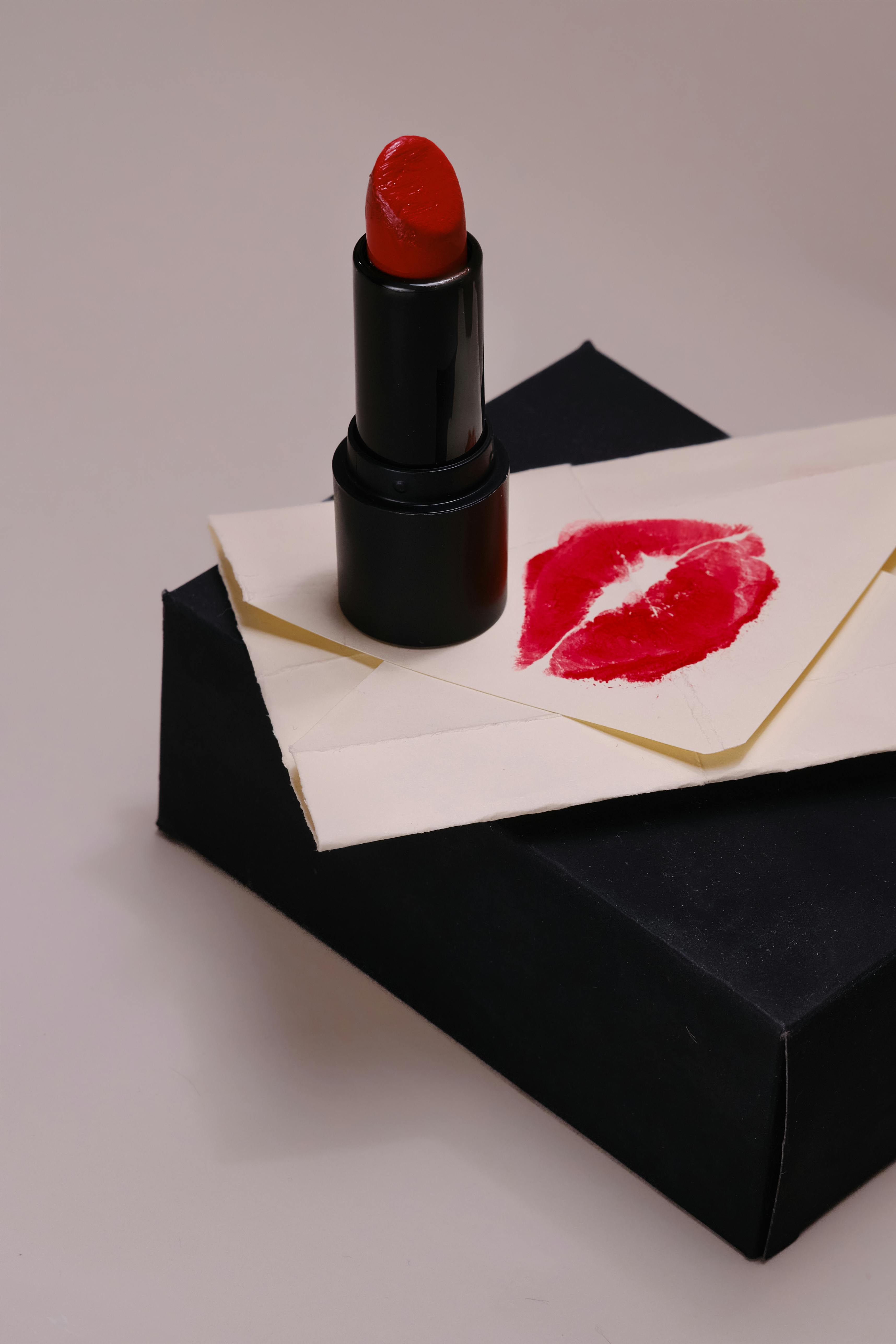 Free Elegant red lipstick with kiss-marked envelope on black box, symbolizing romance and style. Stock Photo