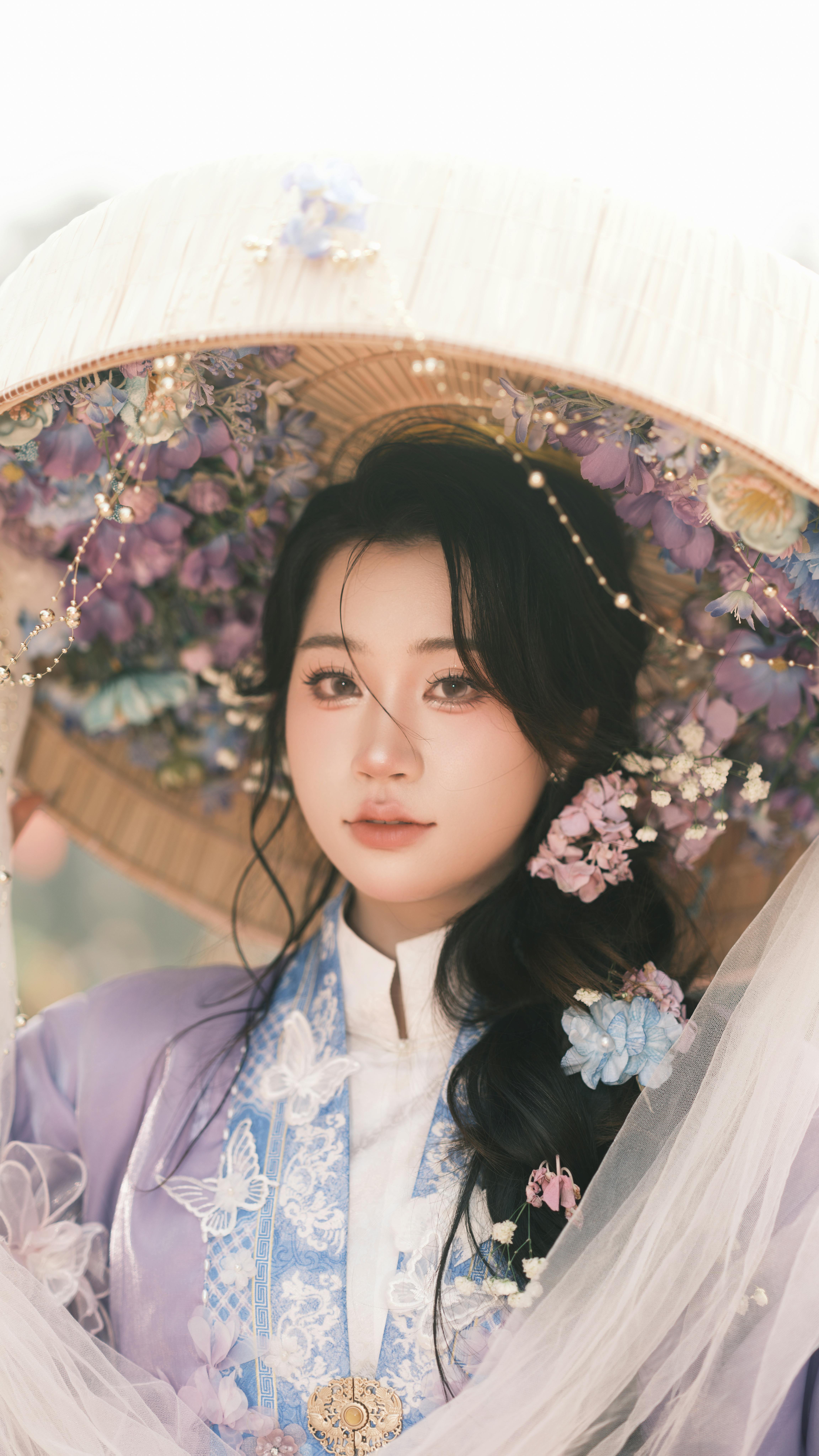 A woman in traditional attire with a floral hat and veil in a soft, dreamy setting.