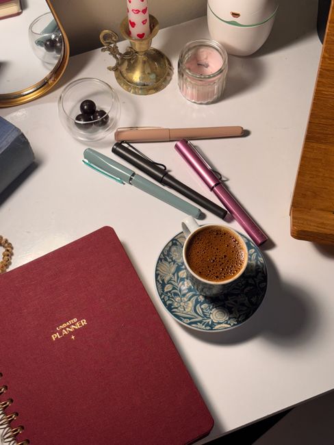 Cozy workspace featuring a coffee cup, planners, and colorful pens on a desk.