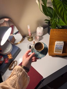 A cozy desk setup with a person holding a cup of coffee surrounded by plants and warm lighting.