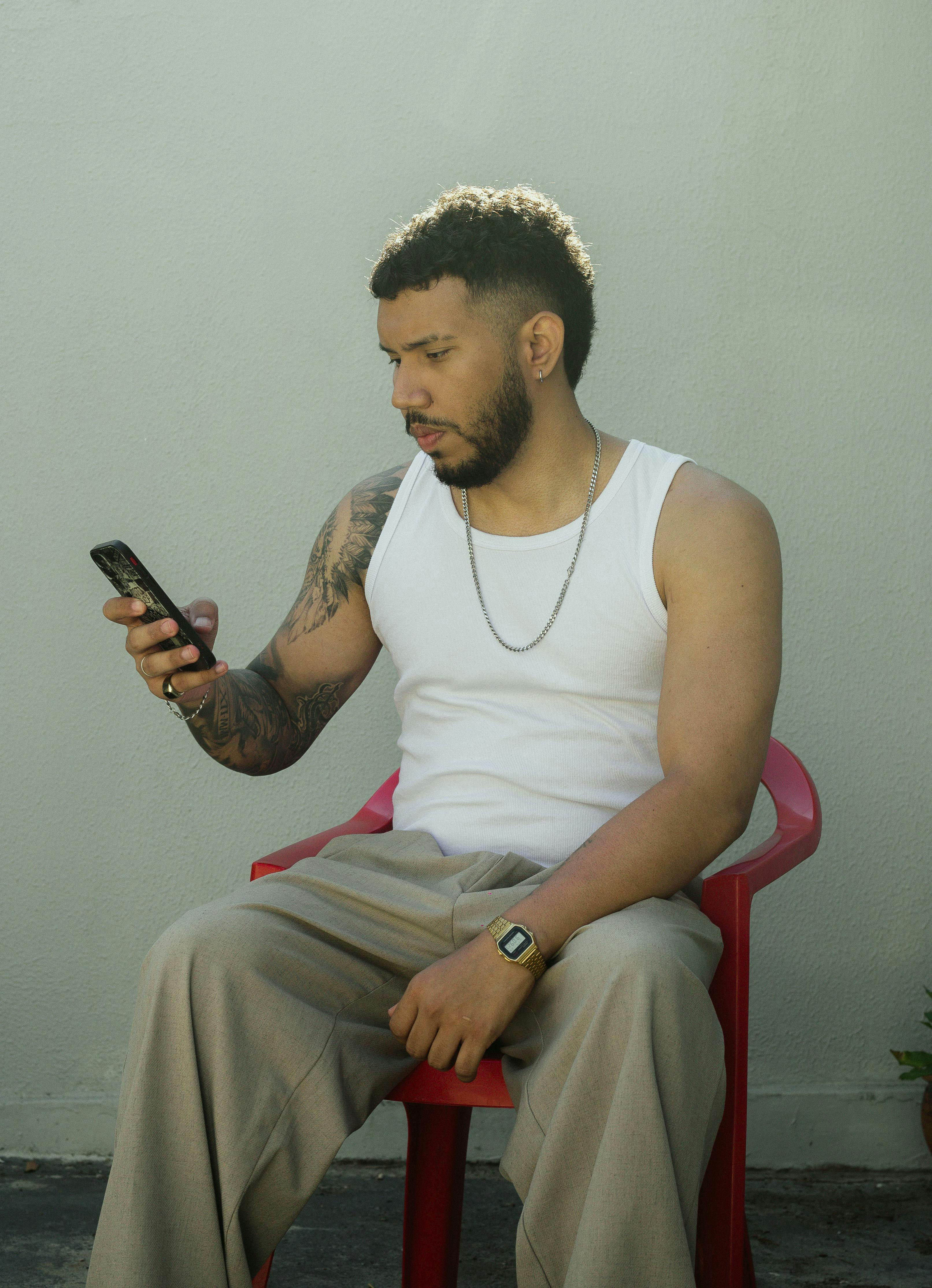 Gratis Un giovane uomo in abbigliamento casual è seduto all'aperto e usa lo smartphone in una giornata di sole. Foto a disposizione