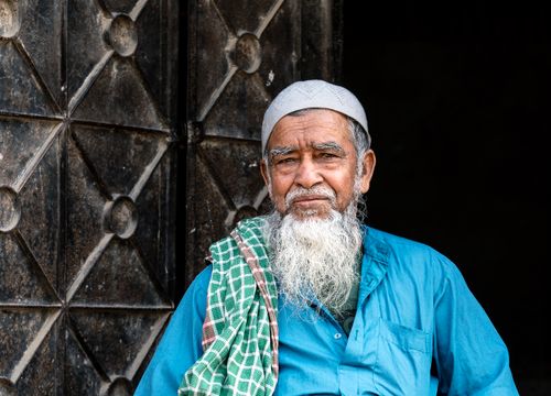 Free Elderly man in traditional attire sitting by a textured door. Stock Photo