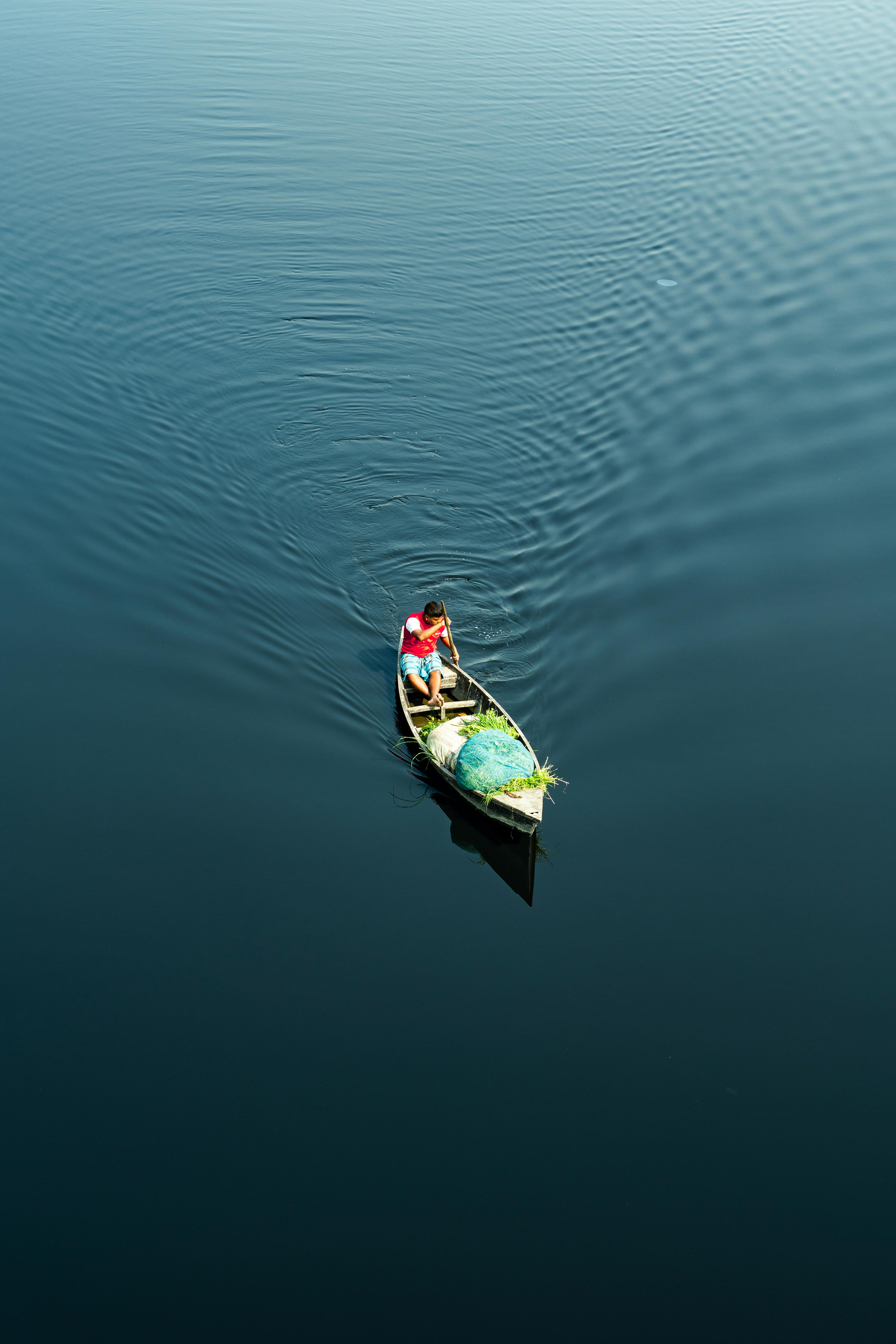 Ücretsiz Sakin bir gölde, bir balıkçı küçük bir kanoyla tek başına kürek çekiyor ve suda hafif dalgalanmalar yaratıyor. Stok Fotoğraflar