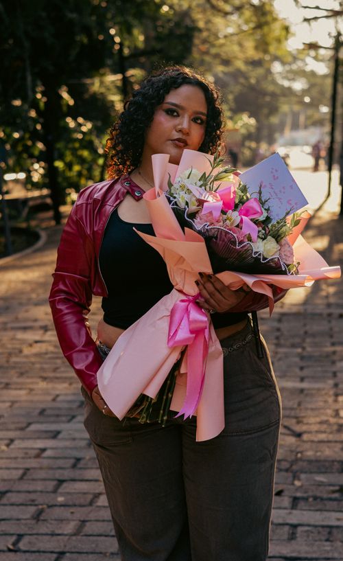 Free Confident woman in urban setting posing with vibrant bouquet under warm sunlight. Stock Photo