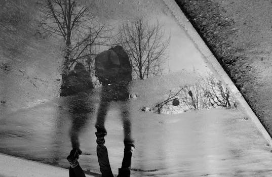 Artistic reflection of two people walking by trees in a puddle. Moody and abstract imagery.
