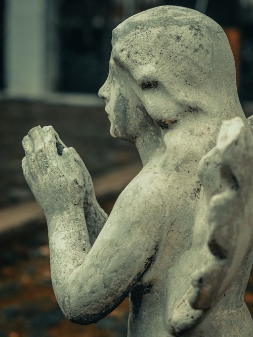 Free A detailed side view of a weathered stone angel statue in an outdoor setting. Stock Photo