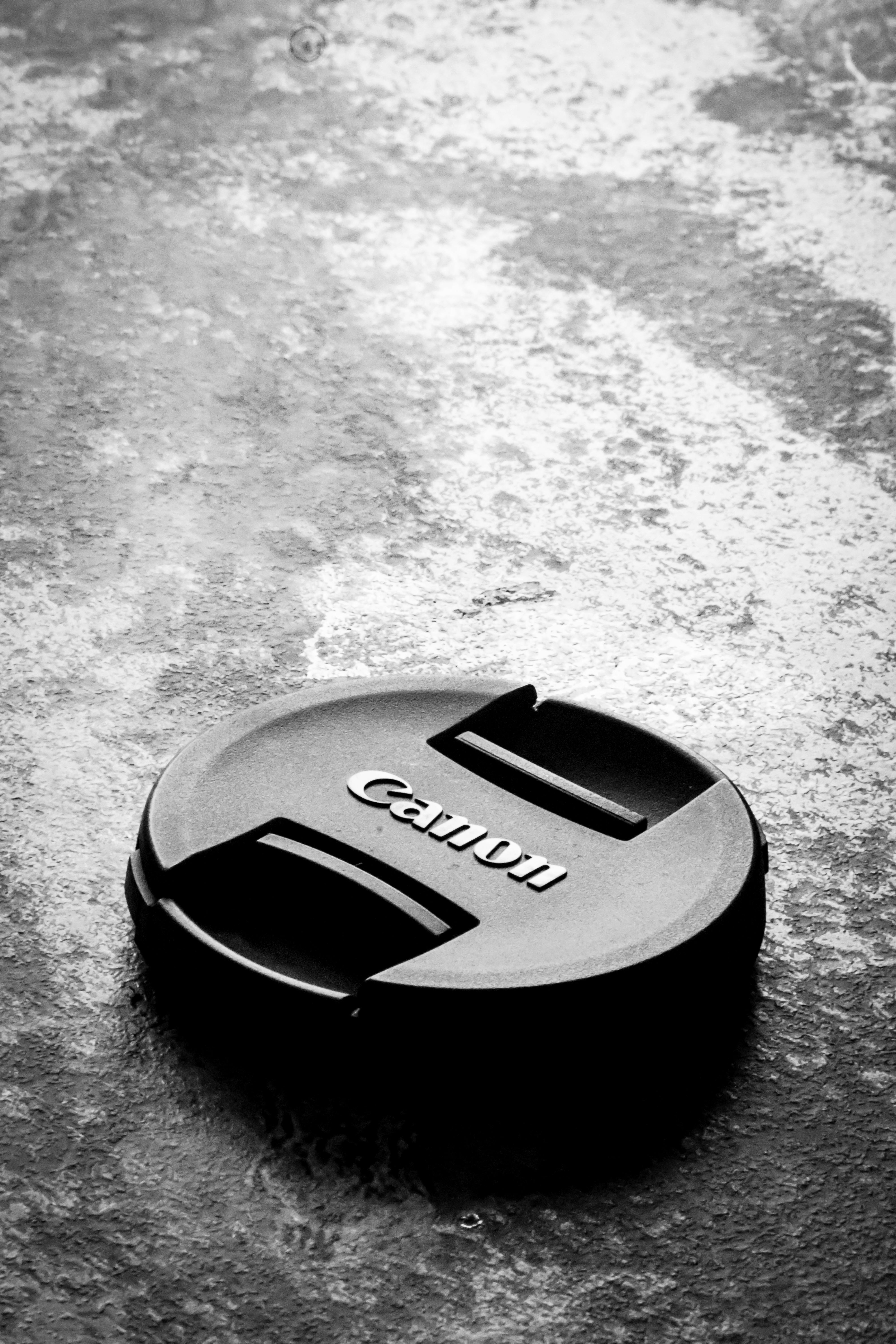 Free Black camera lens cap on reflective wet surface, showcasing photography equipment essentials. Stock Photo