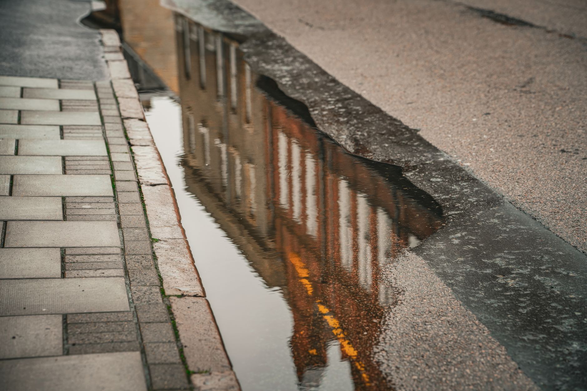 Urban architecture beautifully reflected in a street puddle with textured road and sidewalk.