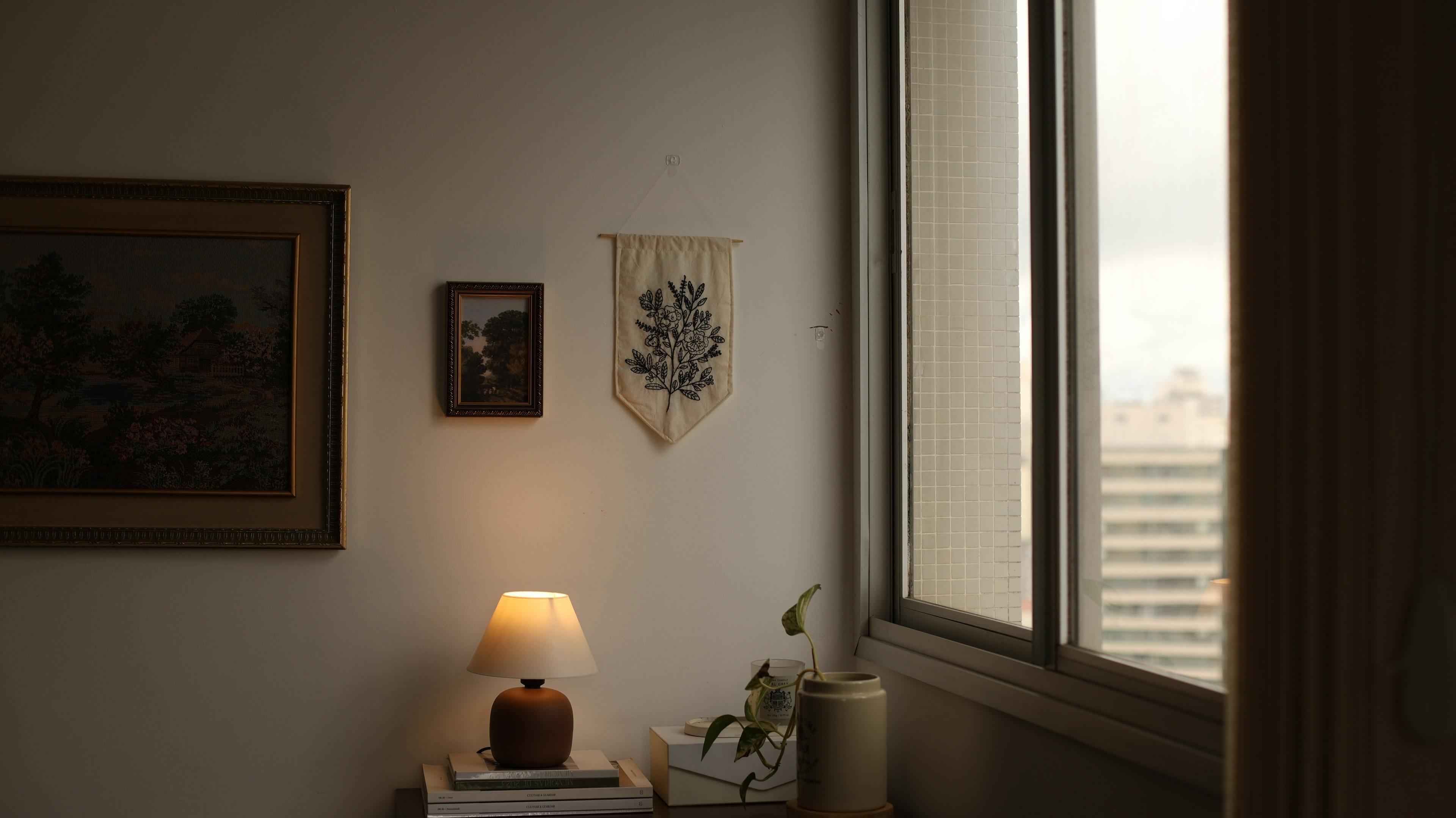 bezplatná Teplá vnitřní scéna s lampou, rostlinami, uměním a výhledem na město z okna. Základová fotografie