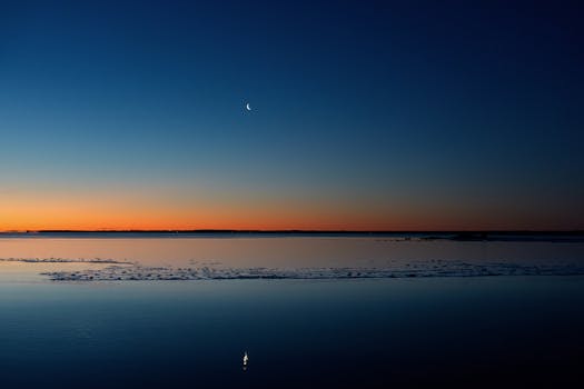 Tranquil winter sunrise at Cove Island Park showcasing a crescent moon over icy waters in Stamford, Connecticut.