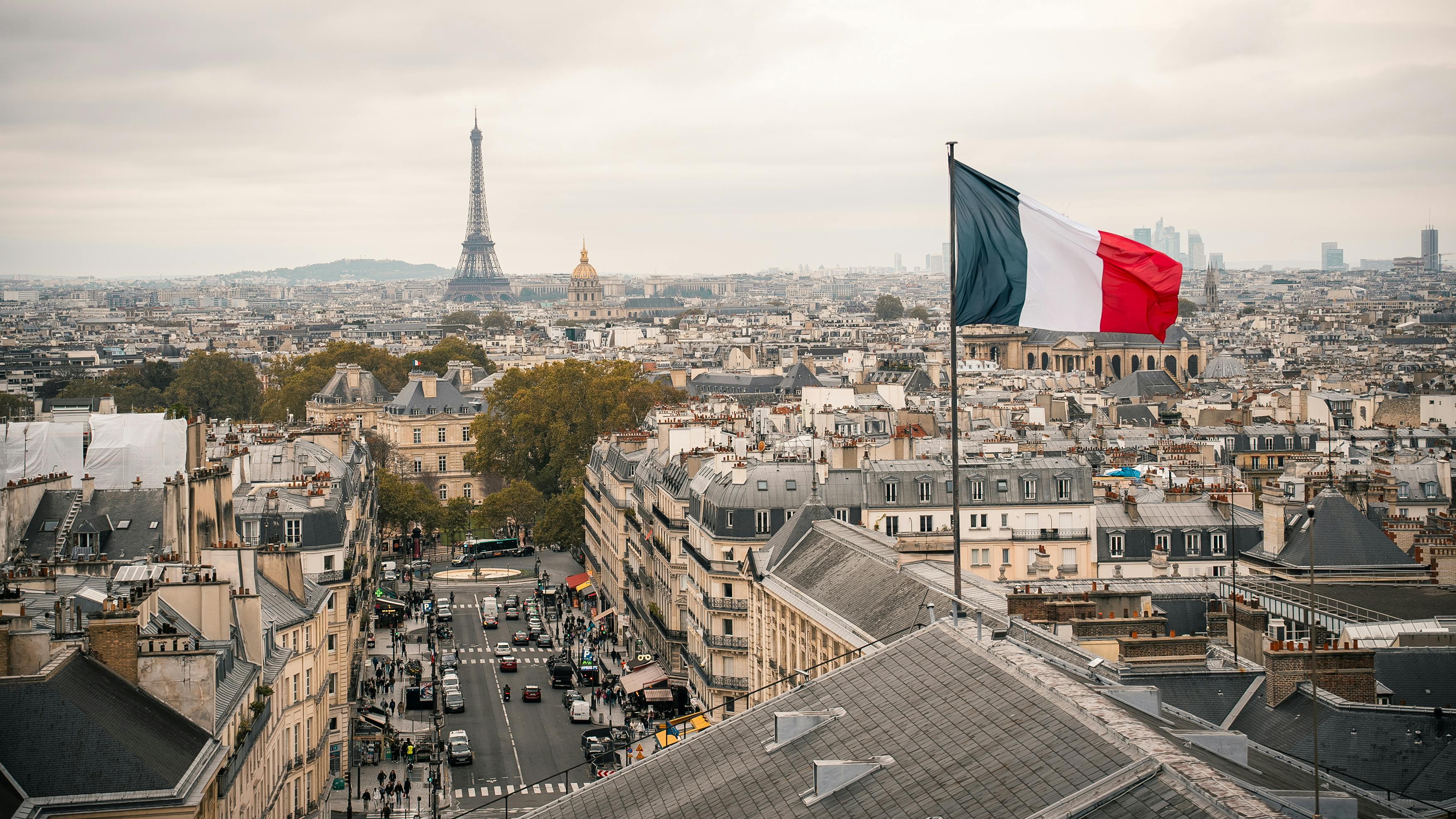 ingyenes Párizs látképének légi felvétele az Eiffel-toronnyal és a város felett lengető, kiemelkedő francia zászlóval. Stockfotó