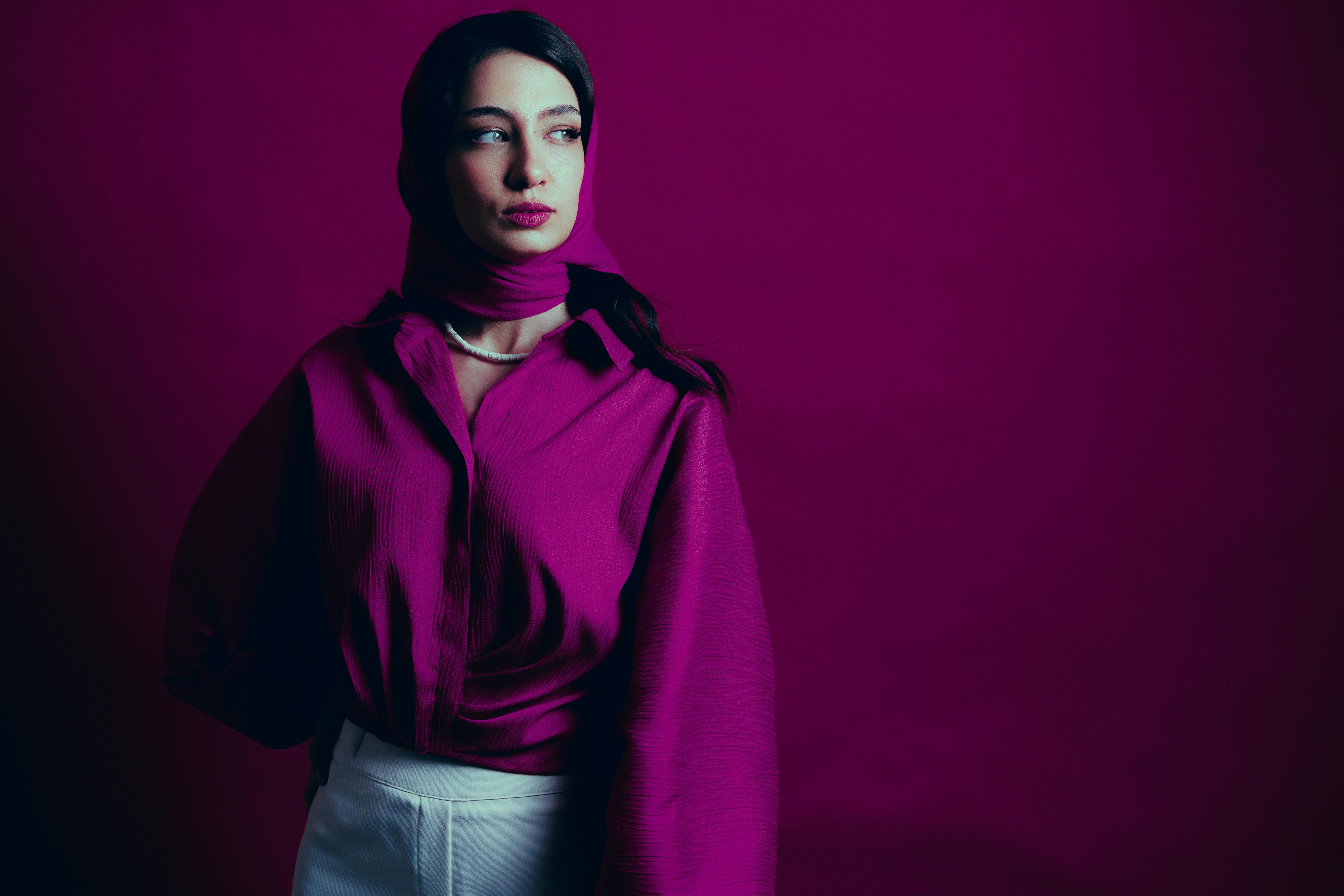 Gratis Donna elegante che indossa un top e una sciarpa color magenta e guarda di lato, con uno sfondo vivace. Foto a disposizione