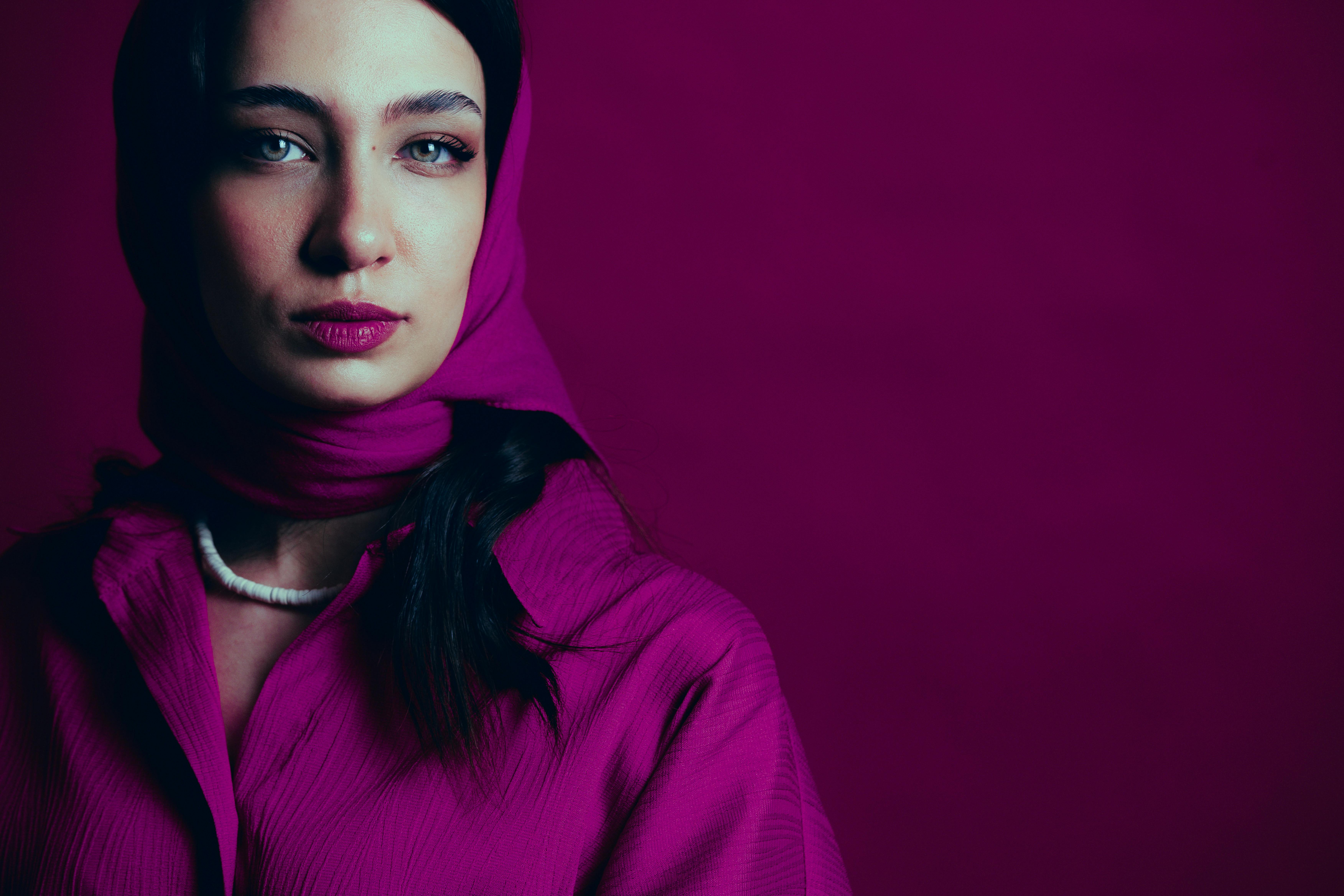 Close-up portrait of a woman wearing a magenta hijab against a matching background.