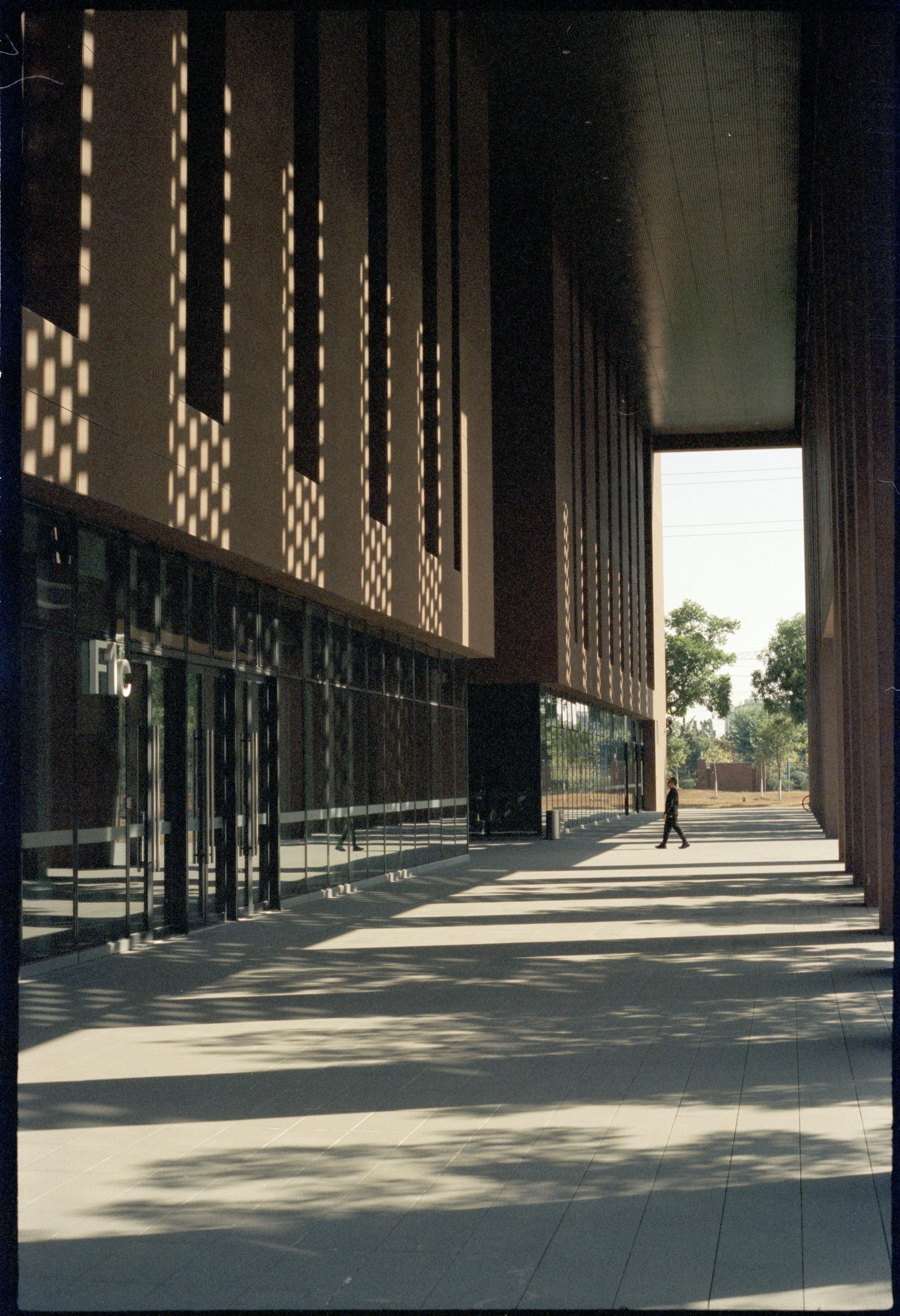 Gratis Fachada de edificio alto con sombras llamativas y figura solitaria caminando. Foto de stock
