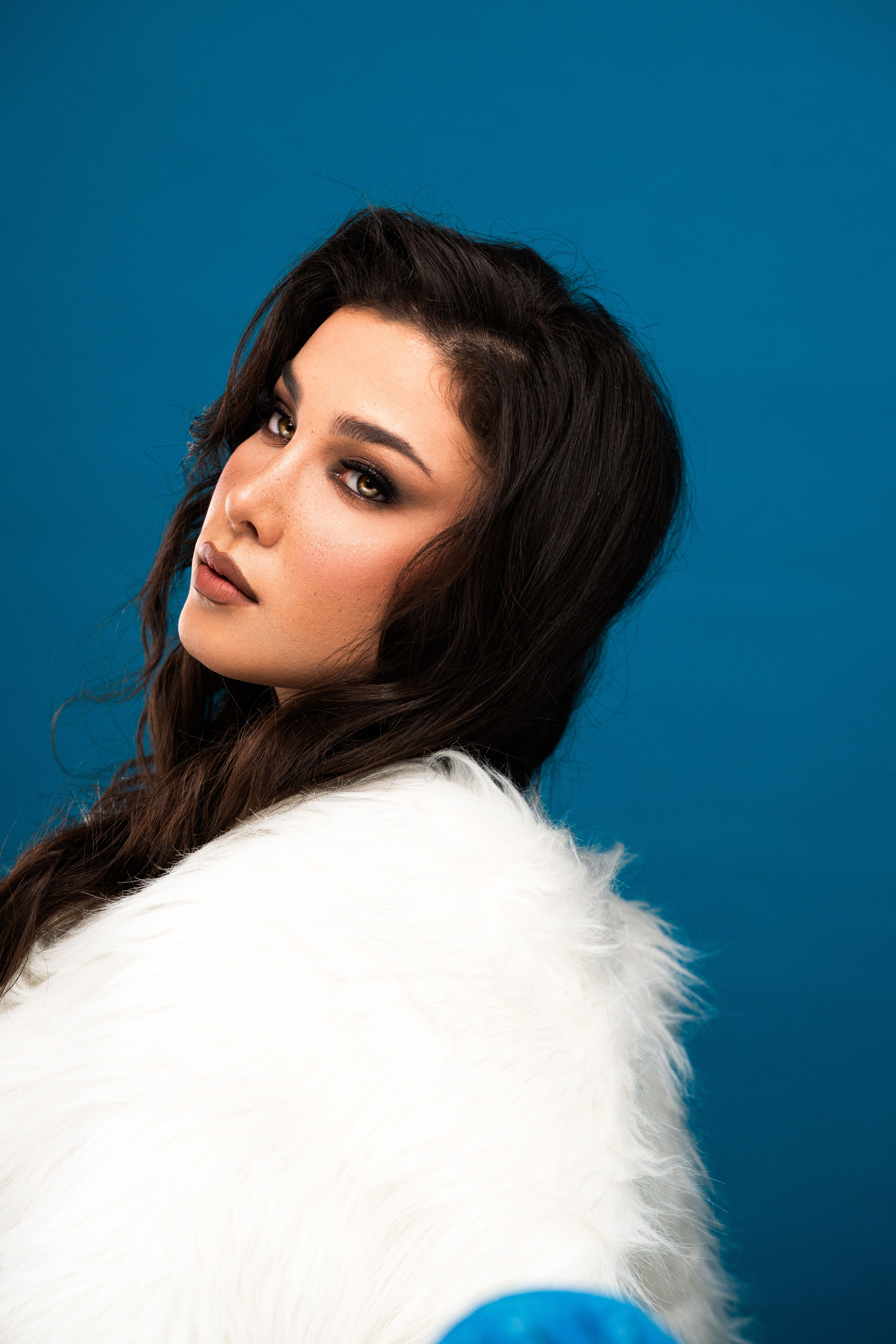 Stunning portrait of a woman wearing white fur with a vivid blue background.