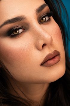 Striking close-up portrait of a woman with bold makeup against a blue background.