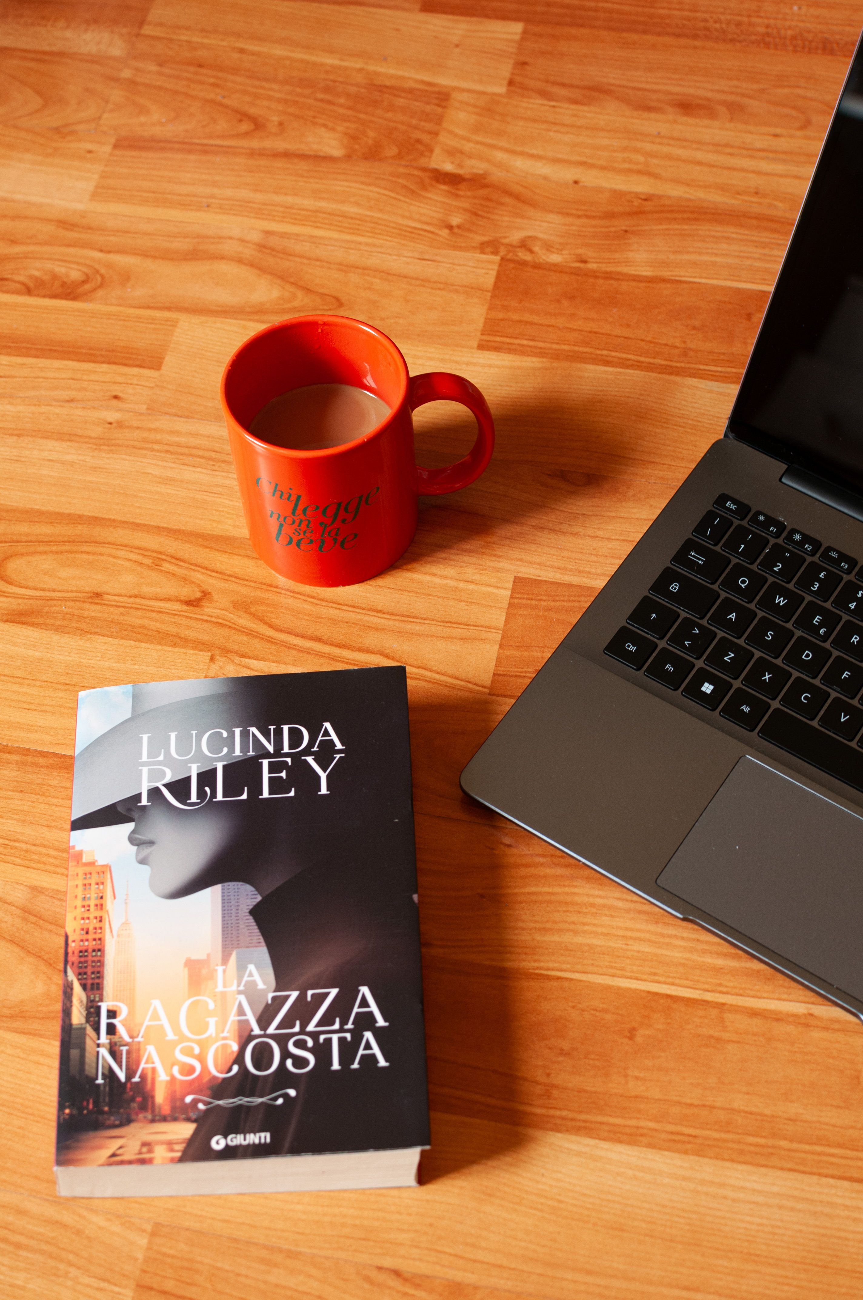 Warm and inviting reading spot with a book, coffee mug, and laptop on wooden floor.