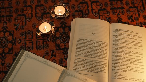 Open book with candles on a patterned rug creating a warm, cozy ambiance.