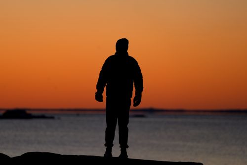 Free A lone figure silhouetted against a vibrant winter sunrise along the Stamford coastline. Stock Photo