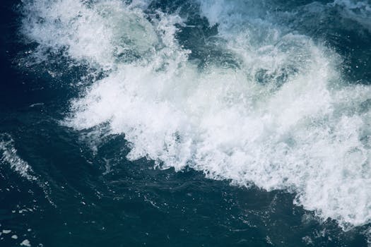 Vibrant ocean wave crashing with frothy foam on the deep blue sea surface, conveying energy and movement.
