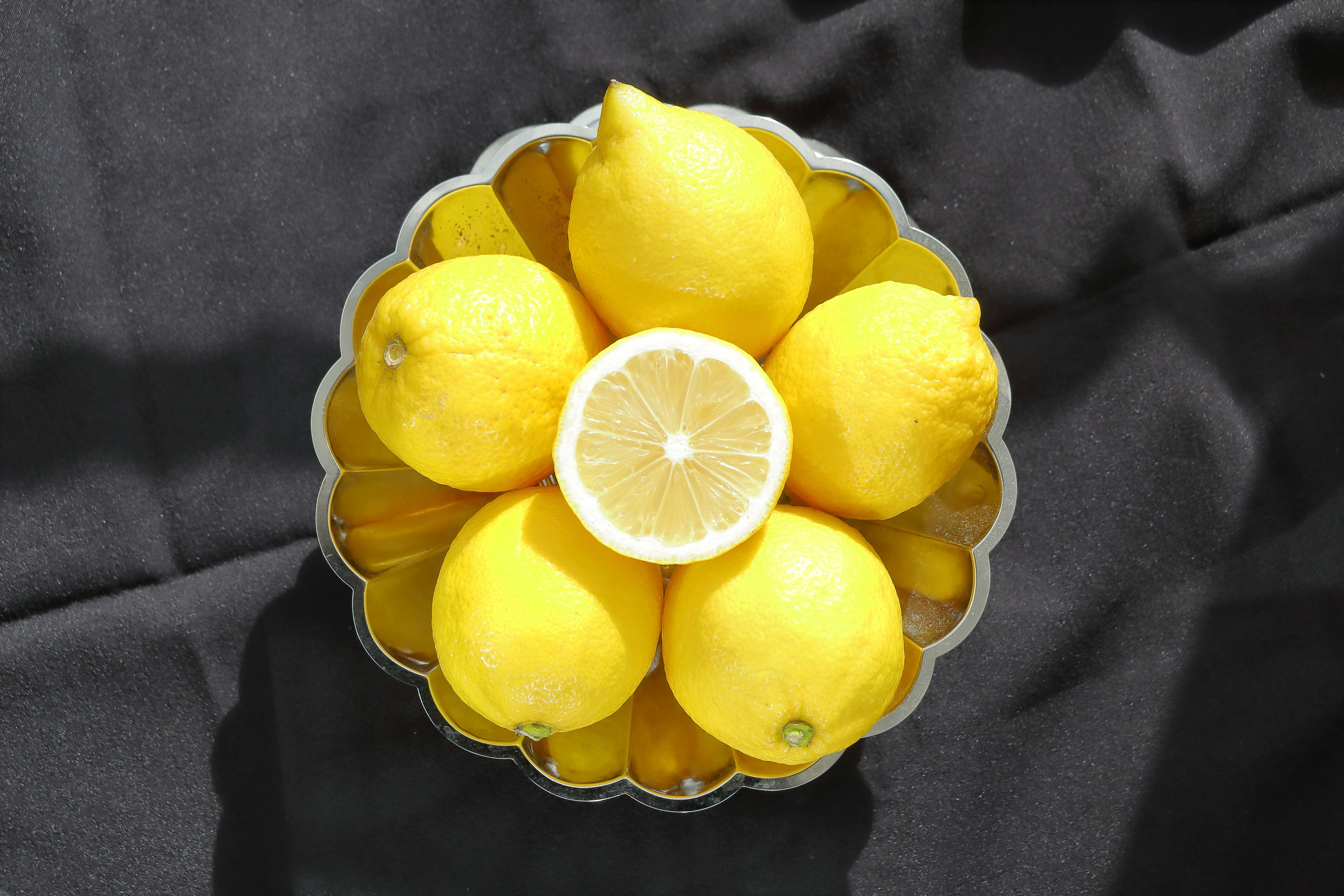 Ücretsiz Siyah kumaş üzerinde metal bir kasede bulunan taze sarı limonların üstten görünümü, canlı ve parlak. Stok Fotoğraflar