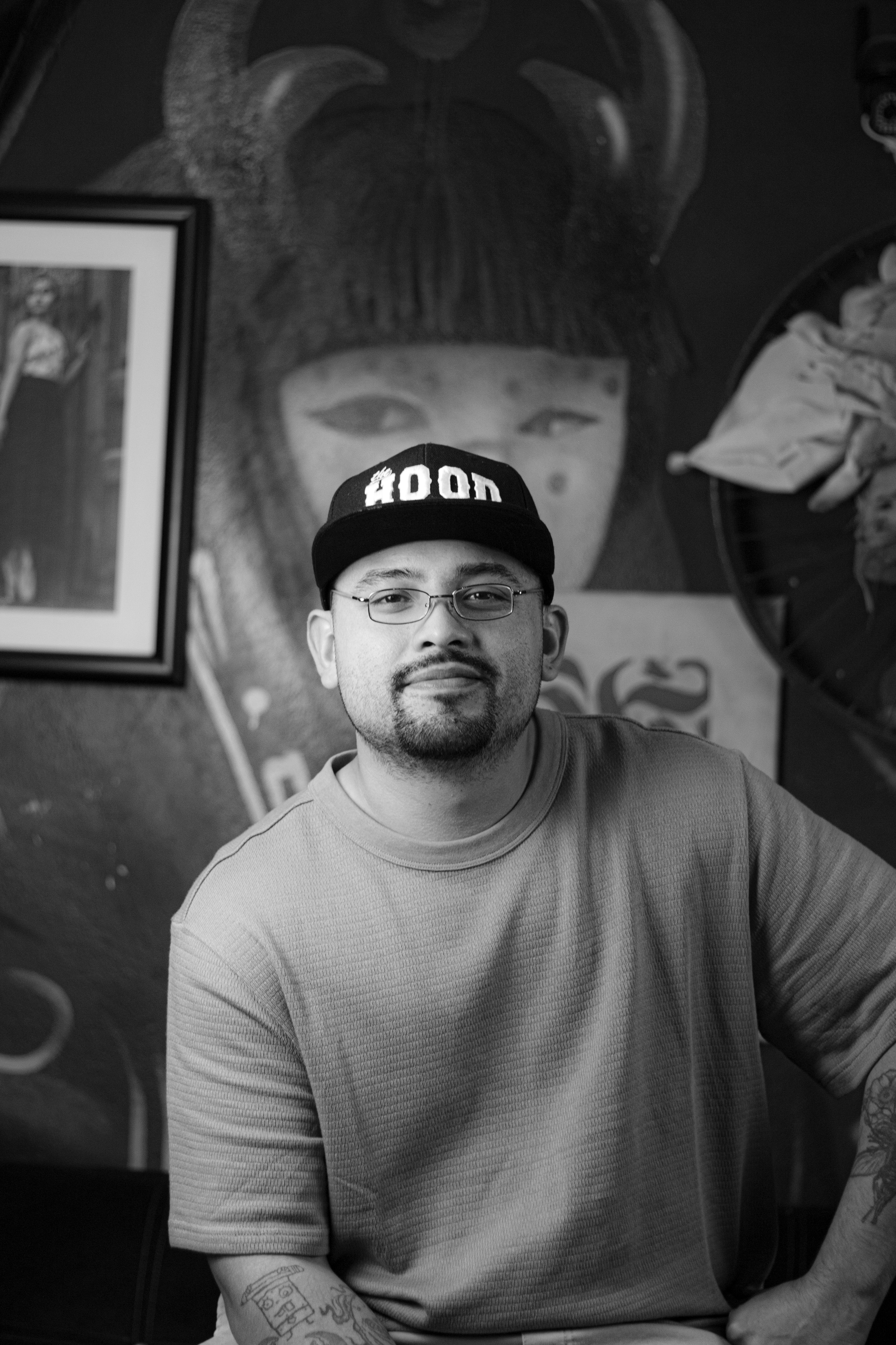 Black and white portrait of a man wearing glasses and a cap in an art studio.