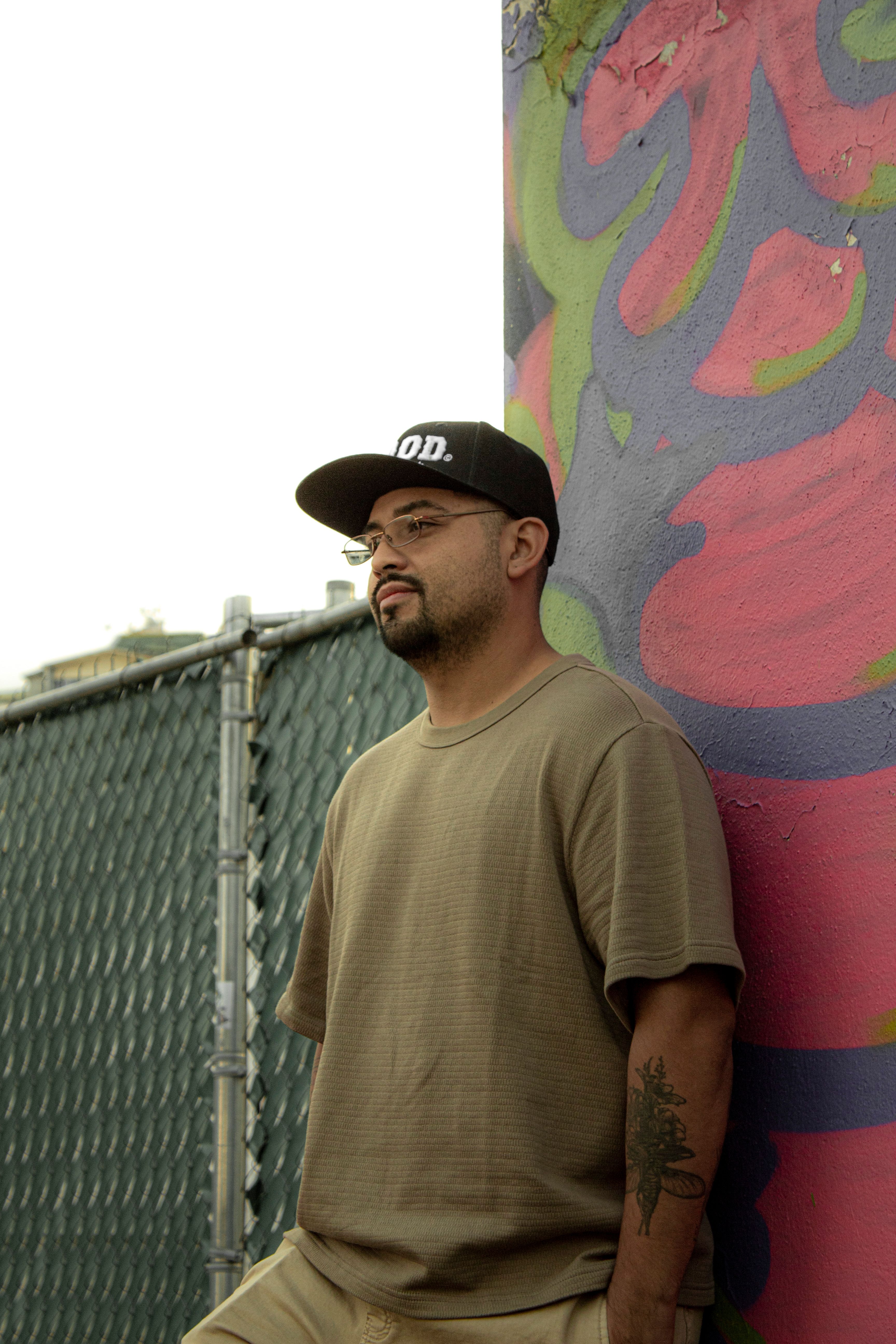 Man wearing a cap and t-shirt stands pensively by a vibrant graffiti wall outdoors in Mexico.