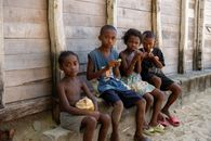 Four children eating lollipops sit by a wooden building in Madagascar.