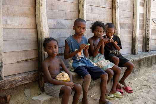 Four children eating lollipops sit by a wooden building in Madagascar.