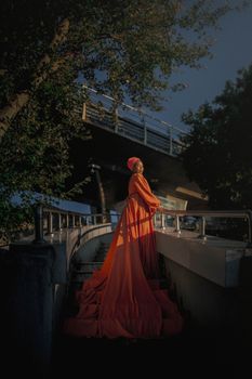 A woman in a stunning orange gown stands gracefully on a staircase in Istanbul, Türkiye.