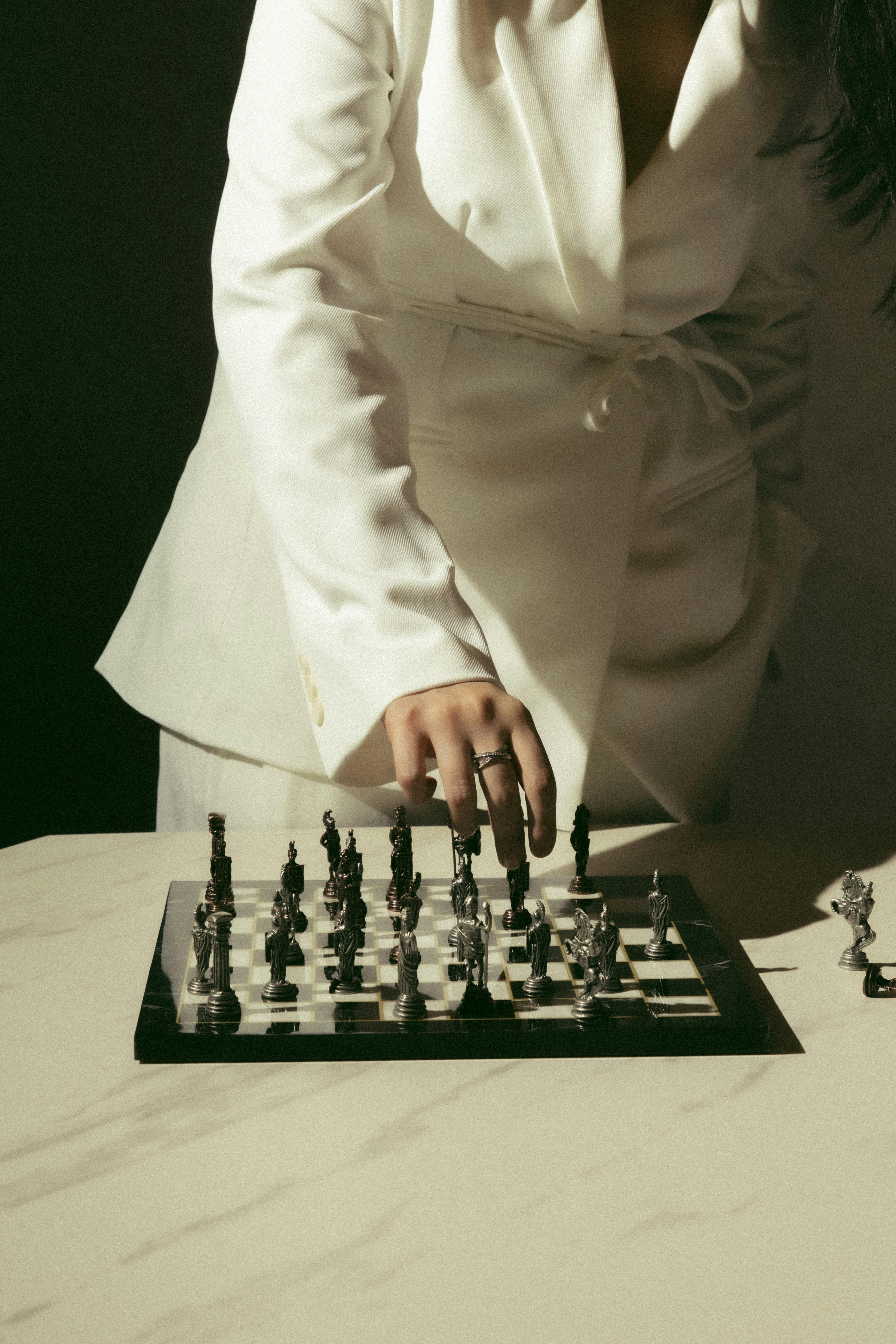 Gratis Una donna in carriera in abito bianco gioca a scacchi, simboleggiando il processo decisionale strategico. Foto a disposizione