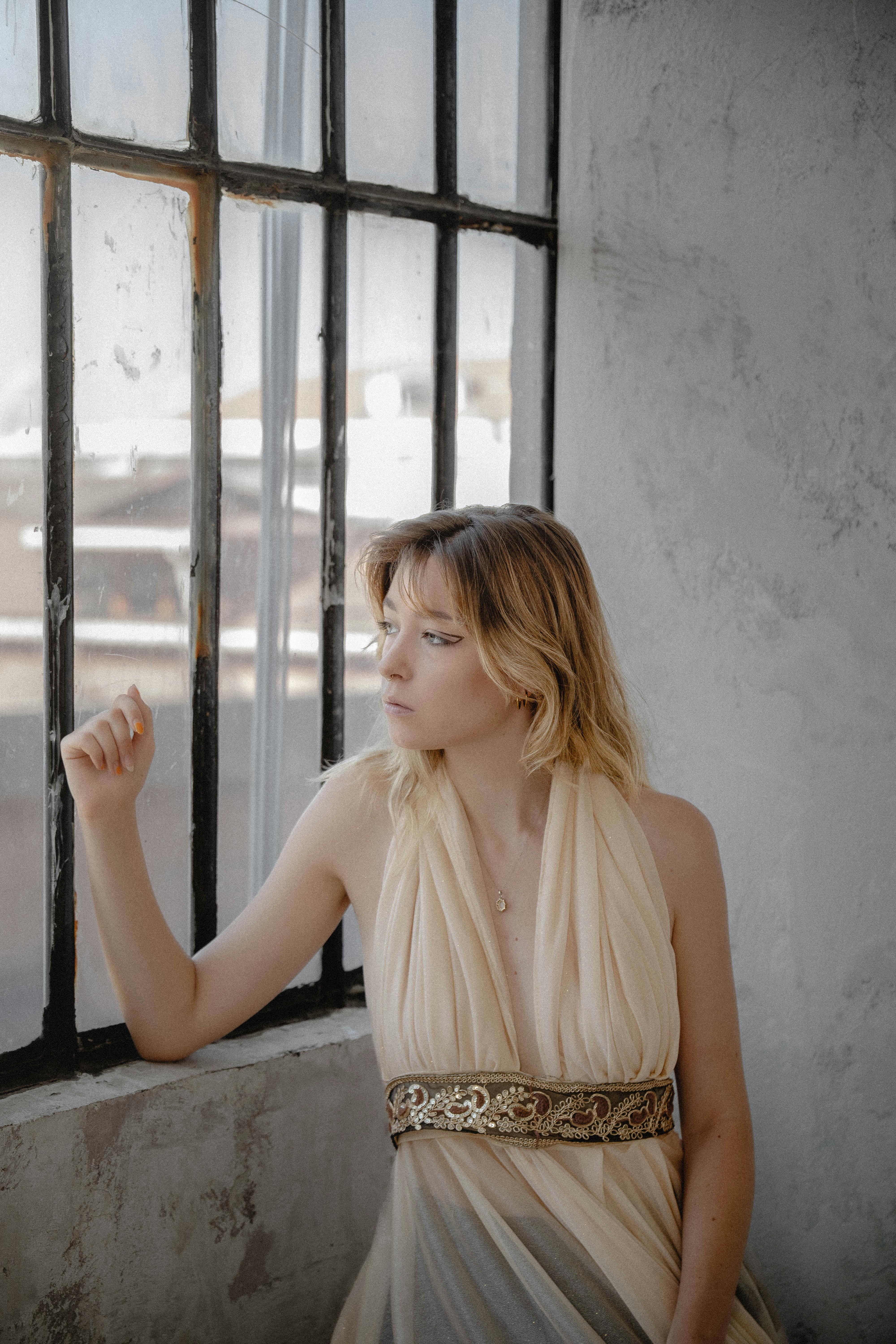 Gratis Donna pensierosa in abito elegante che guarda fuori da una finestra industriale a Istanbul, Turchia. Foto a disposizione