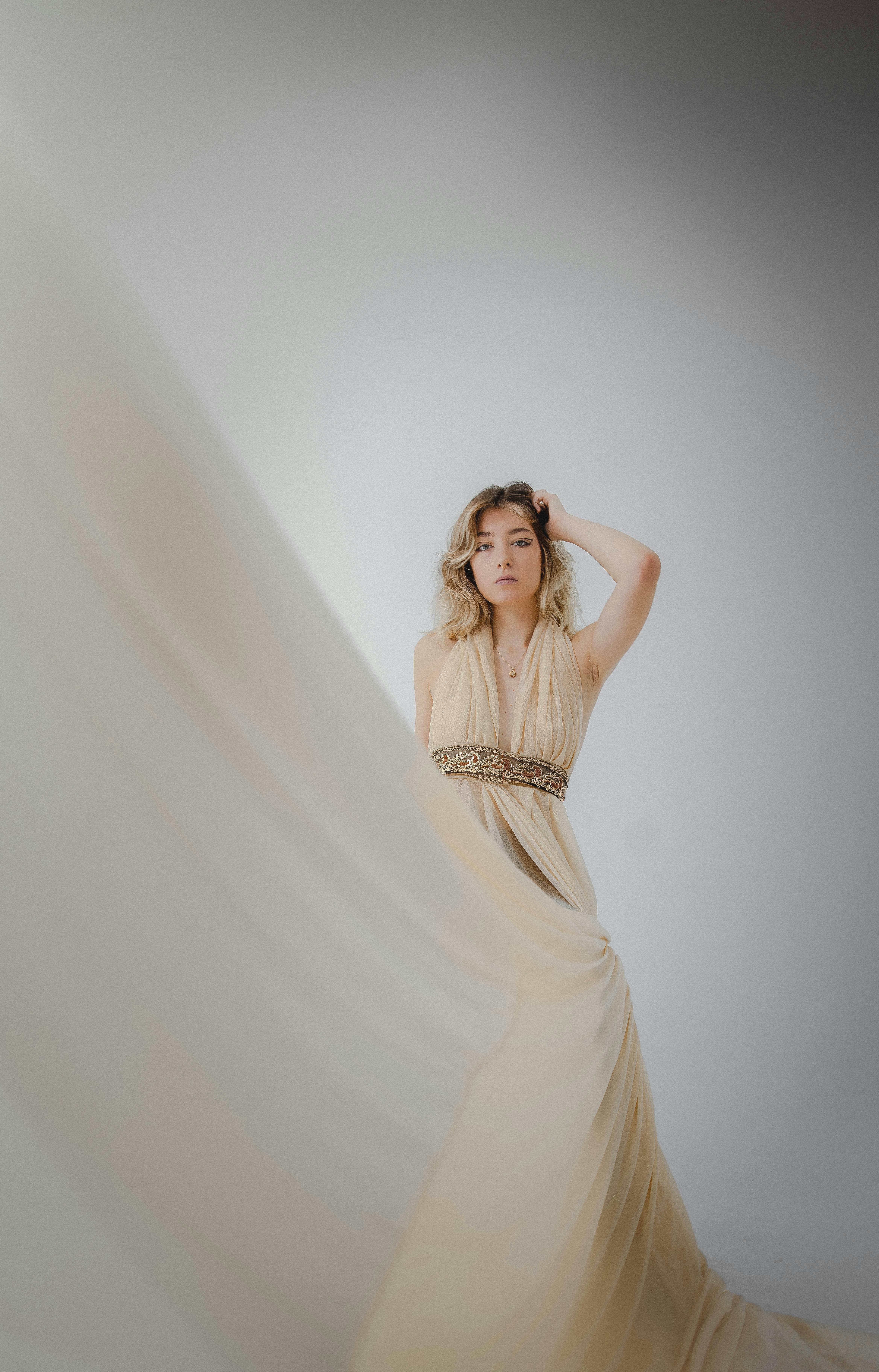 Ilmainen Nainen poseeraa sulavasti sisätiloissa hulmuavassa beigenvärisessä mekossa, jossa on sileää kangasta. Kuvapankkikuva