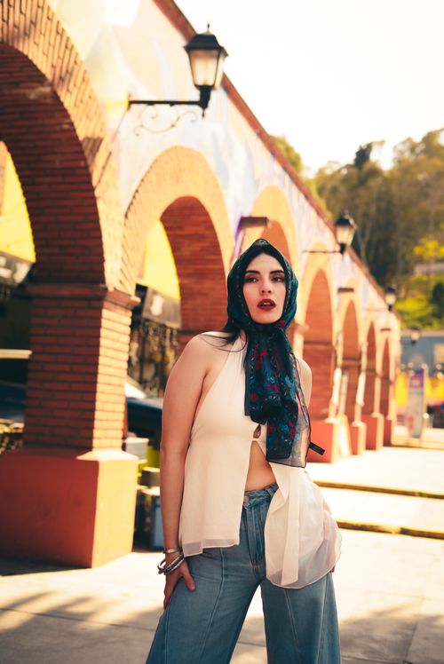 Free Fashionable woman in scarf posing beside colorful arches in daylight. Stock Photo
