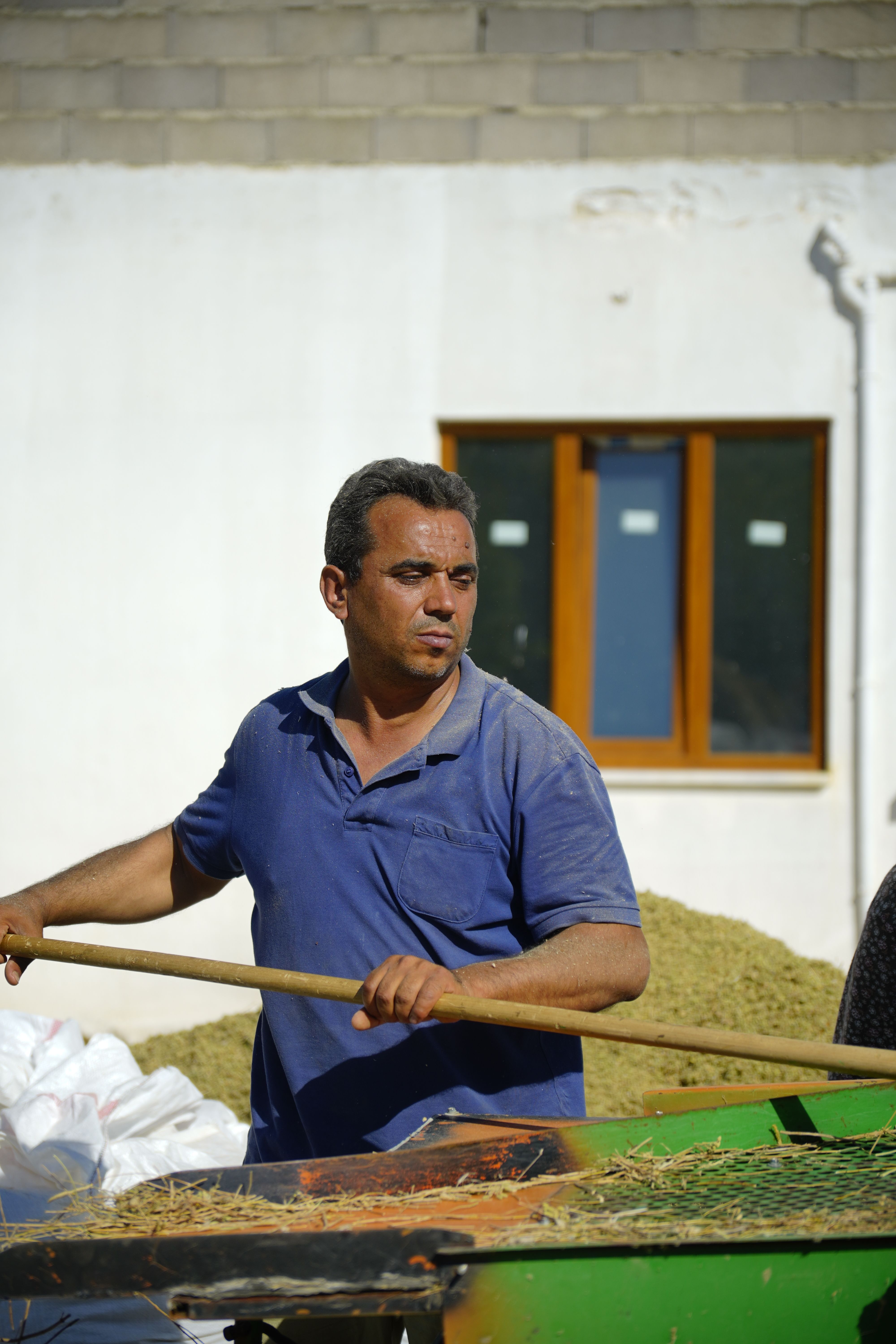 A farmer in Türkiye works outdoors, handling crops with an agricultural tool under the sun.