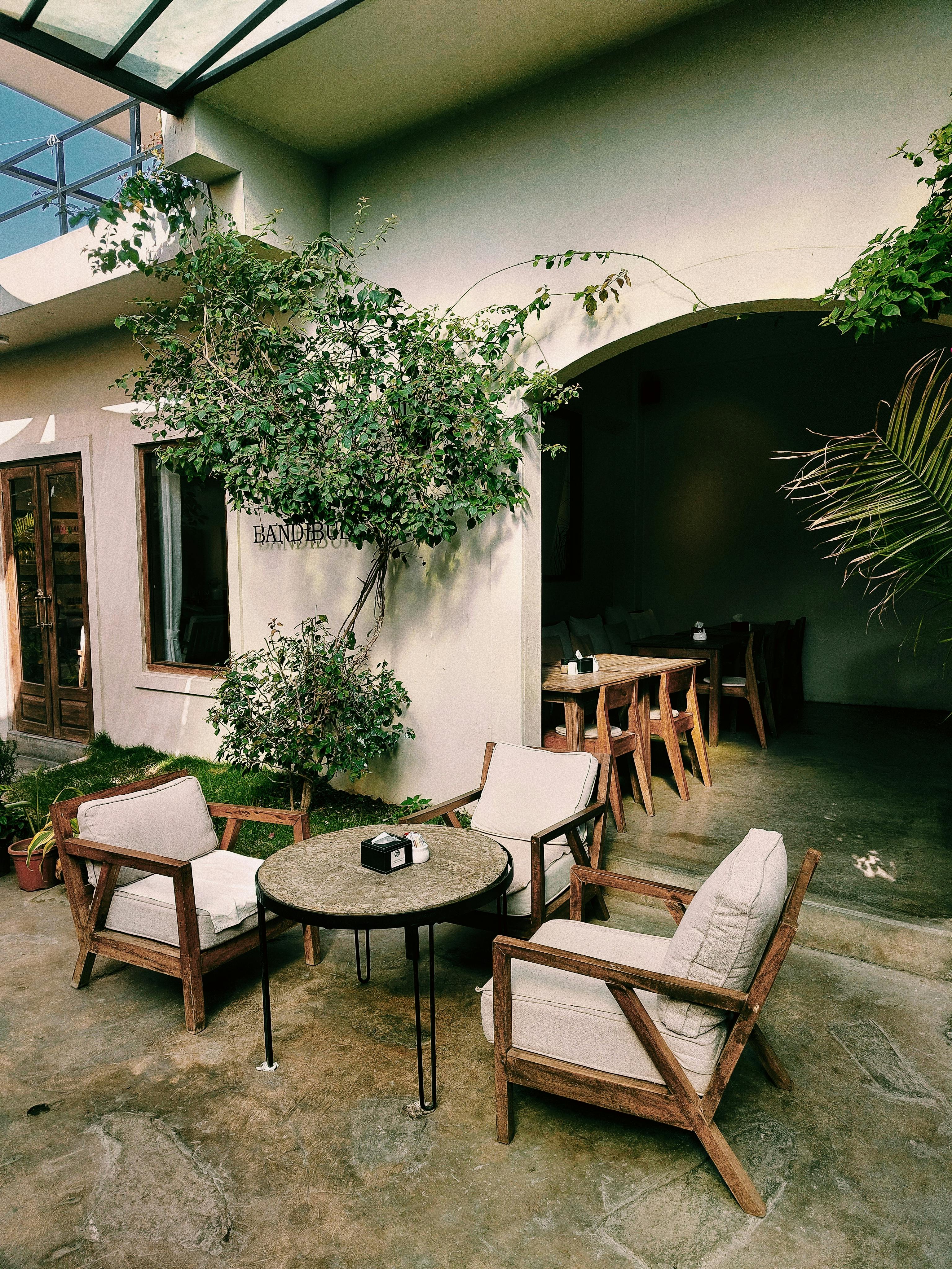 Gratuit Terasă fermecătoare pentru o cafenea în aer liber, cu mobilier din lemn și verdeață luxuriantă. Fotografie de stoc