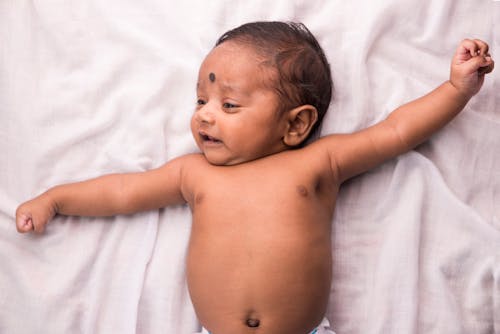 Topless Baby Lying on White Bed