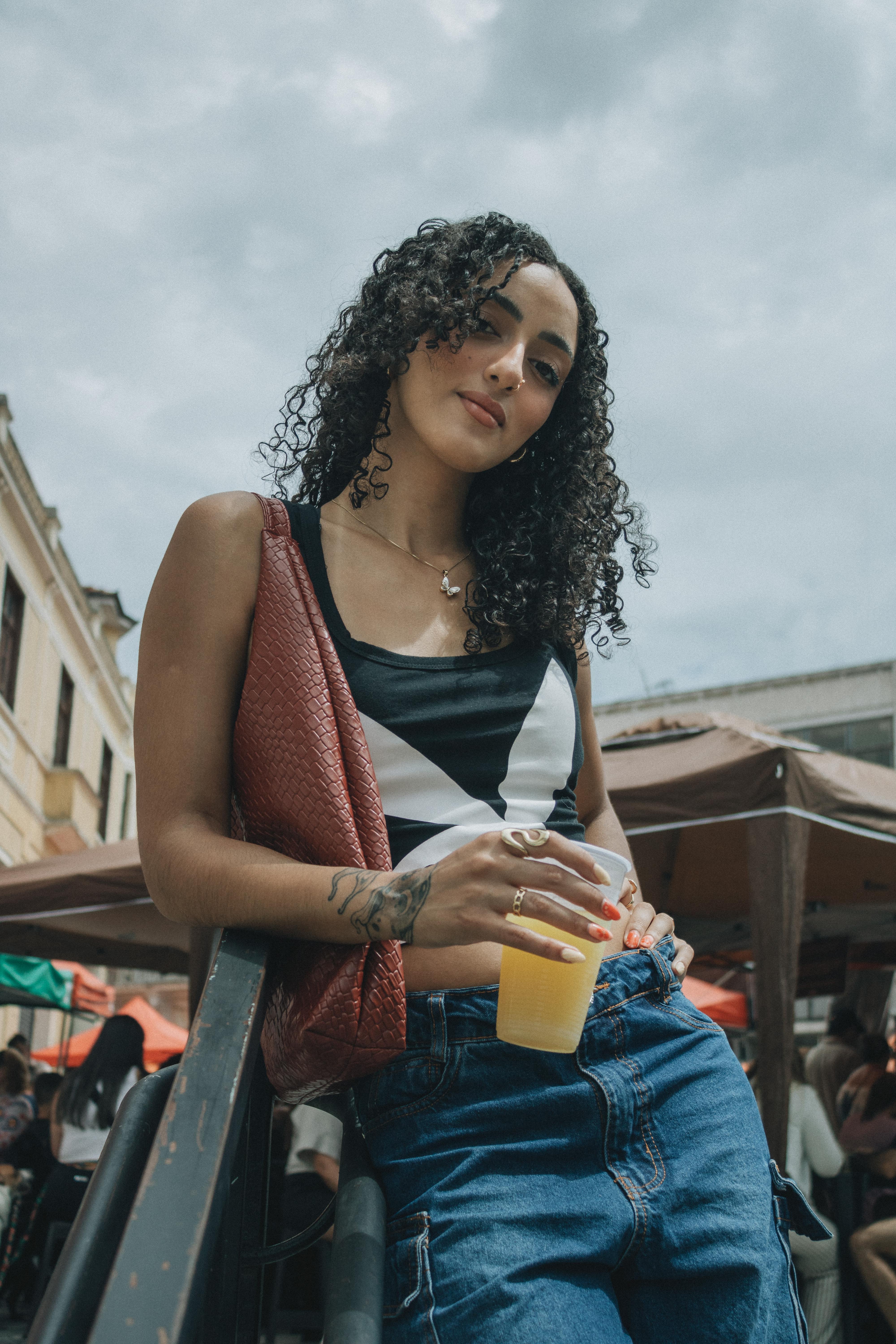 bezplatná Stylová žena s kudrnatými vlasy si venku užívá osvěžující nápoj. Základová fotografie